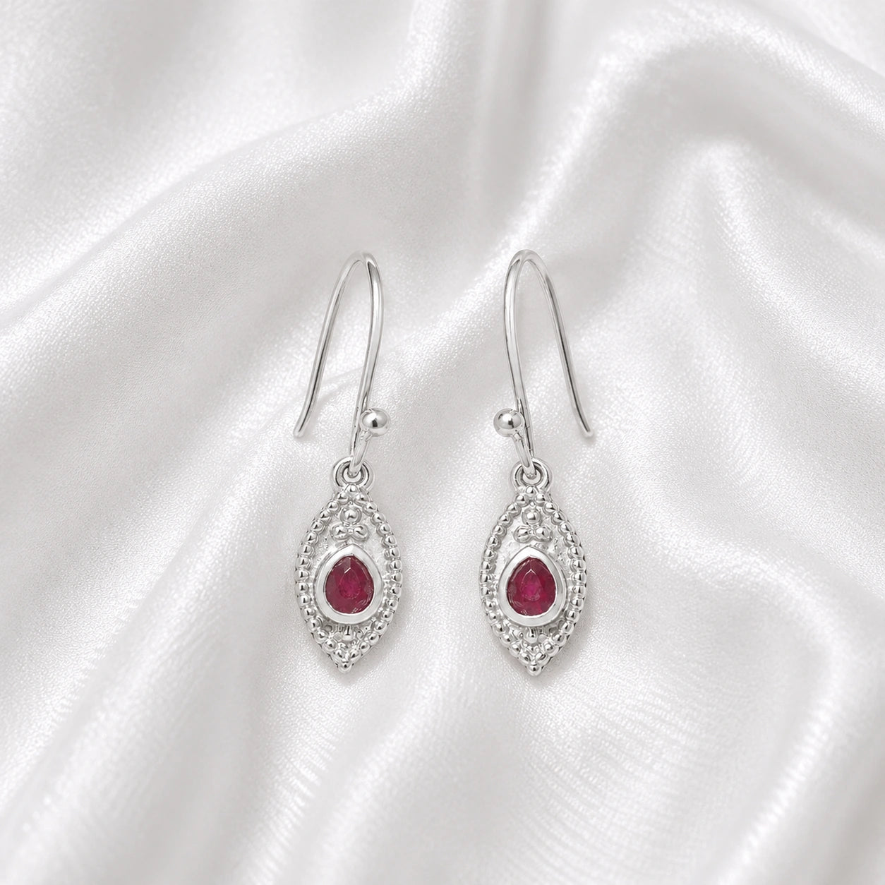 Pink_earrings_in_sterling_silver_with_pear_ruby_stones_at_front_angle_view_on_soft_fabric_background