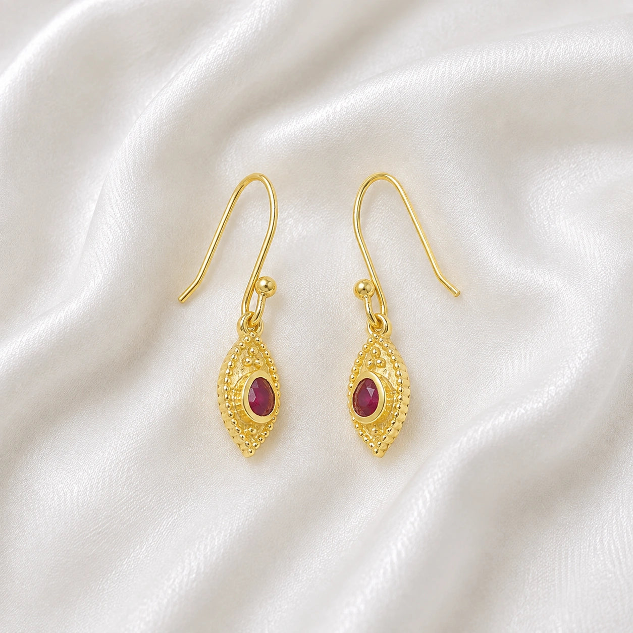 Pink_earrings_in_gold_plated_silver_with_pear_ruby_stones_at_slight_angle_view_on_soft_fabric_background