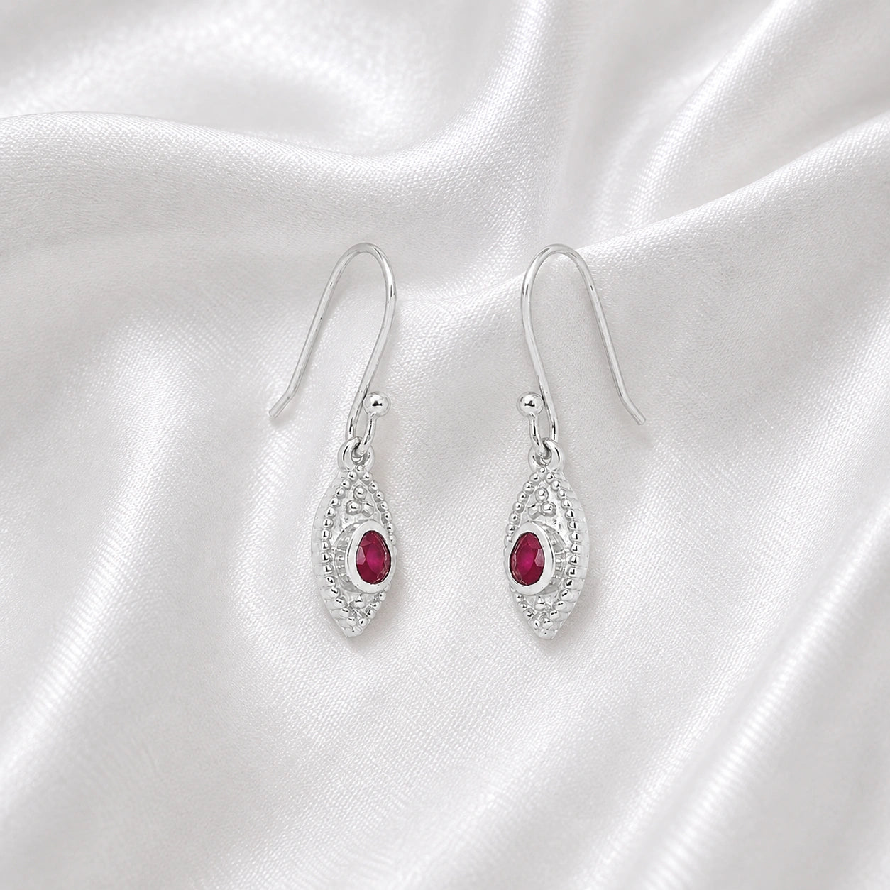 Pink_earrings_in_sterling_silver_with_pear_ruby_stones_at_slight_angle_view_on_soft_fabric_background
