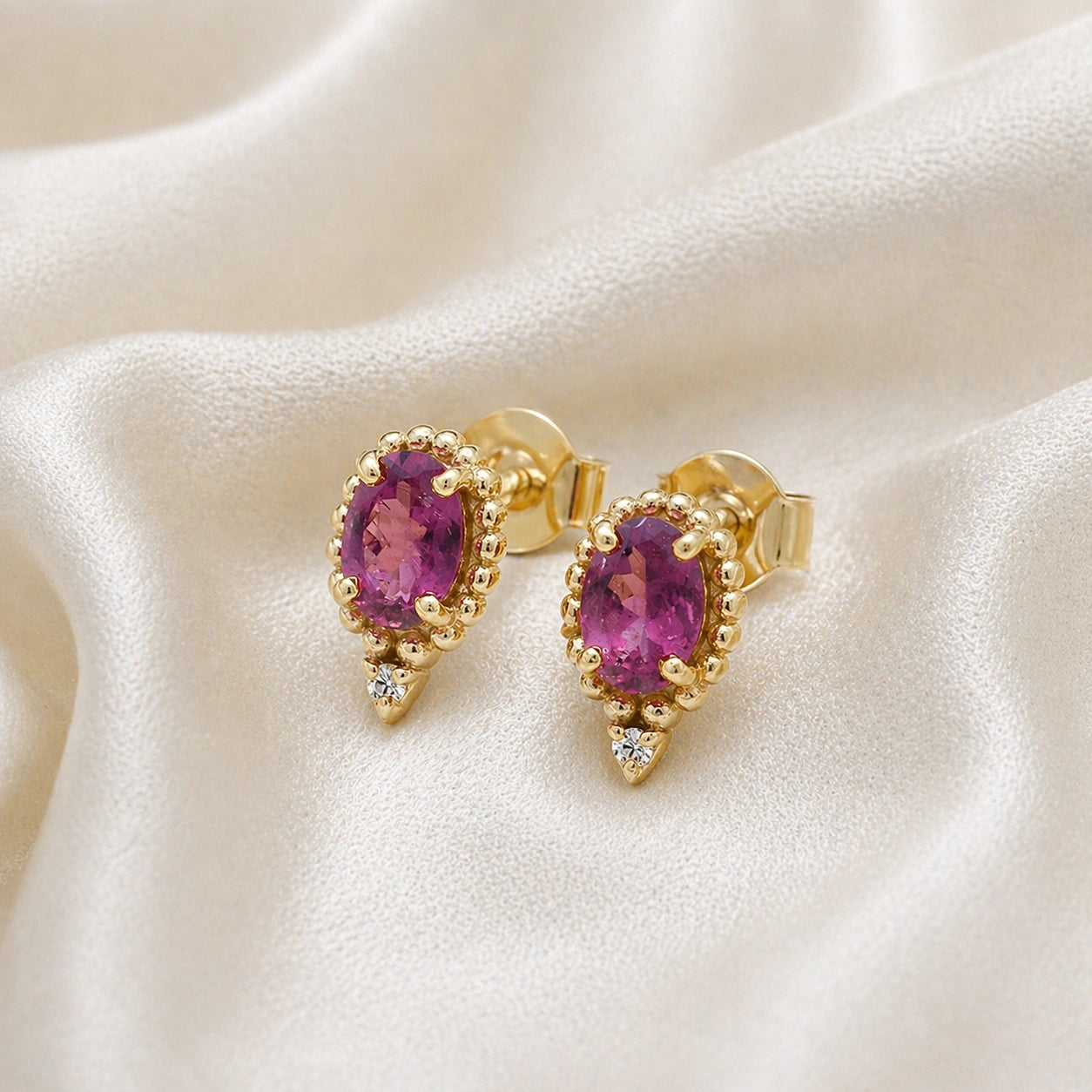 Pink_tourmaline_earrings_in_gold_plated_silver_with_oval_stone_and_a_white_topaz_in_slightly_angle_view_on_soft_fabric_background