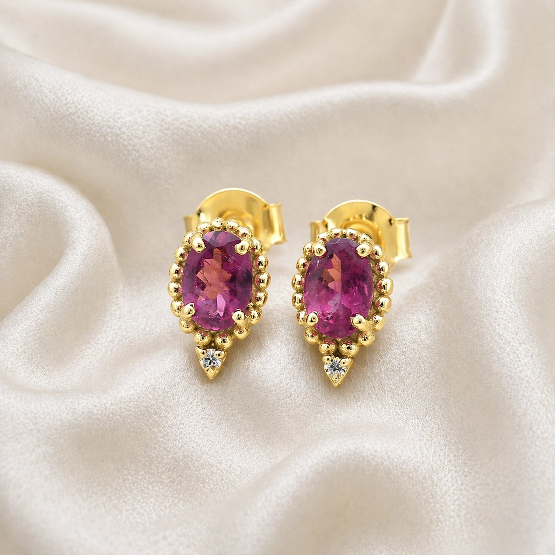 Pink_tourmaline_earrings_in_gold_plated_silver_with_oval_stone_and_a_white_topaz_shown_front_angle_view_on_soft_fabric_background