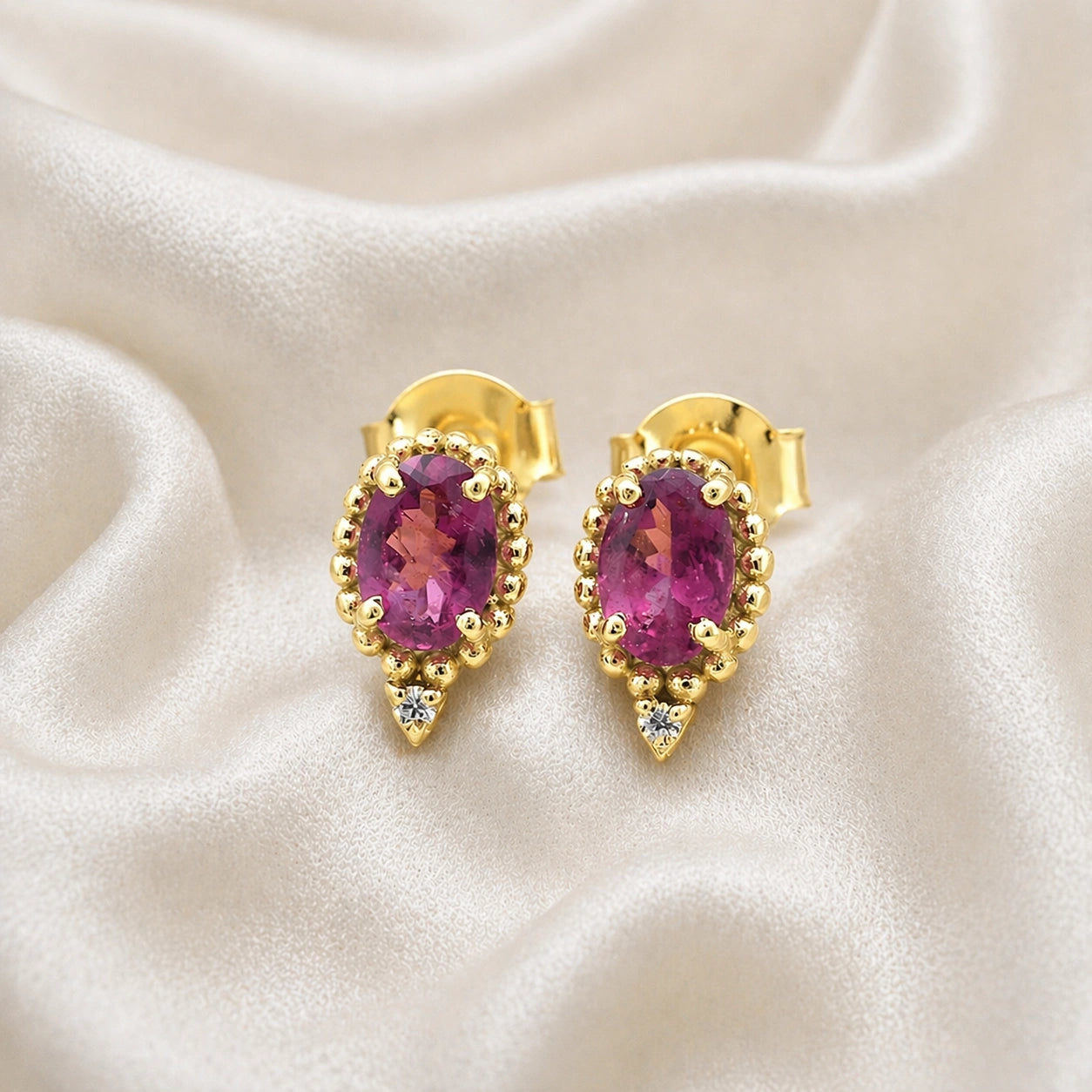 Pink_tourmaline_earrings_in_gold_plated_silver_with_oval_stone_and_a_white_topaz_shown_front_angle_view_on_soft_fabric_background