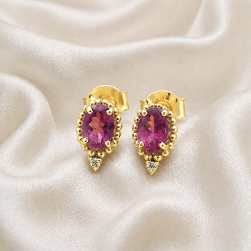 Pink_tourmaline_earrings_in_gold_plated_silver_with_oval_stone_and_a_white_topaz_shown_front_angle_view_on_soft_fabric_background