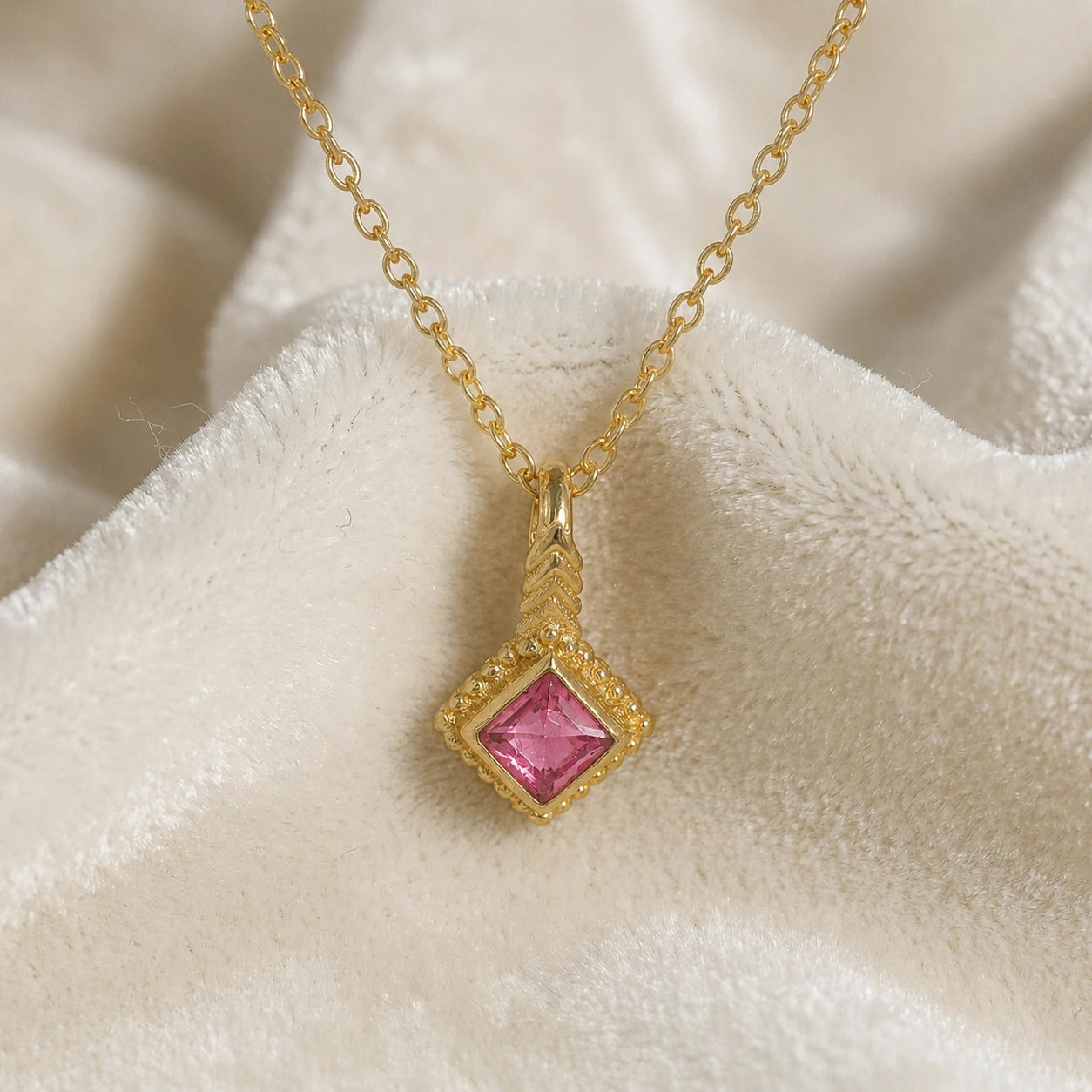 Birthstone_necklace_in_gold_plated_silver_with_square_cut_pink_tourmaline_pendant_in_front_angle_view_on_soft_white_fabric_background