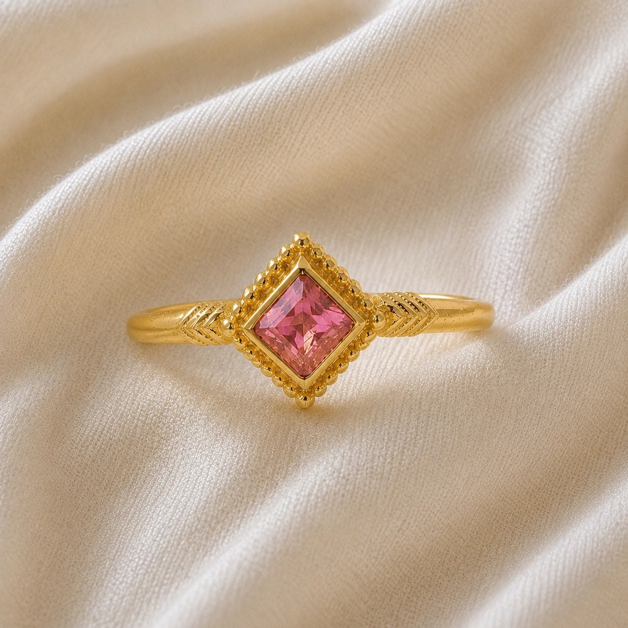 Princess_cut_ring_gold_plated_silver_with_square_pink_tourmaline_and_detailed_band_front_angle_view_on_soft_fabric_background