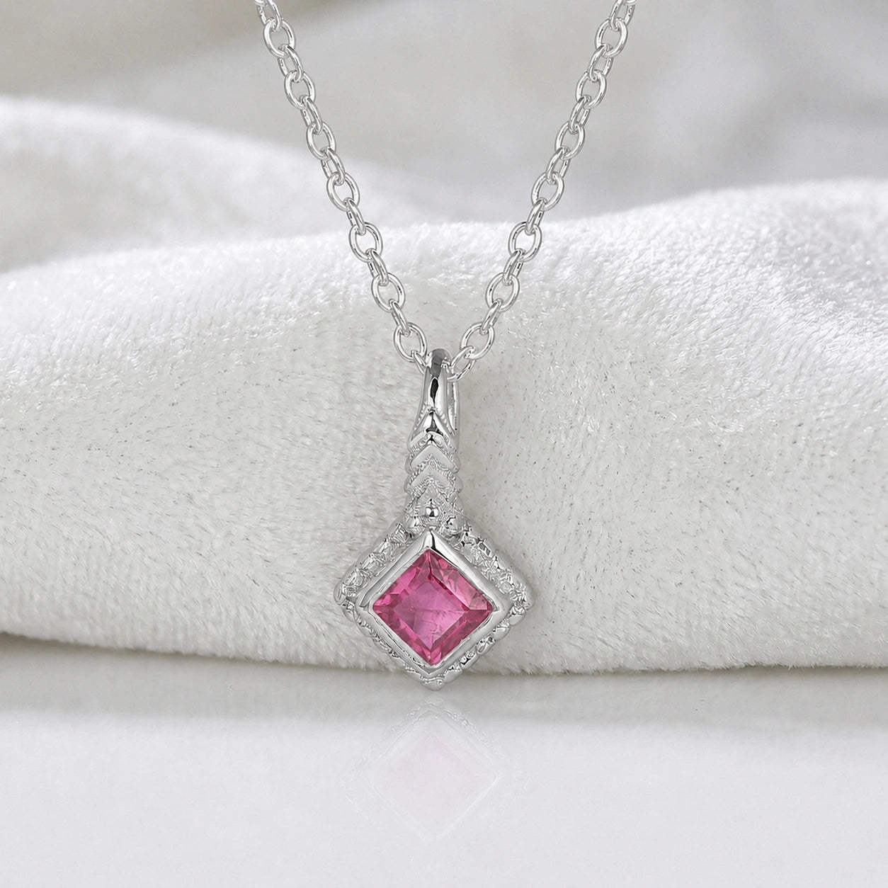 Birthstone_necklace_in_sterling_silver_with_square_cut_pink_tourmaline_pendant_in_front_angle_view_on_soft_white_fabric_background