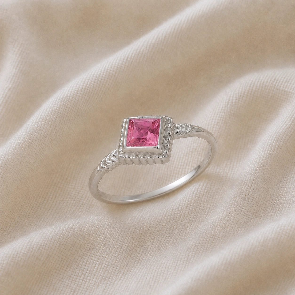 Princess_cut_ring_sterling_silver_with_square_pink_tourmaline_and_detailed_band_slightly_tilted_view_on_soft_fabric_background