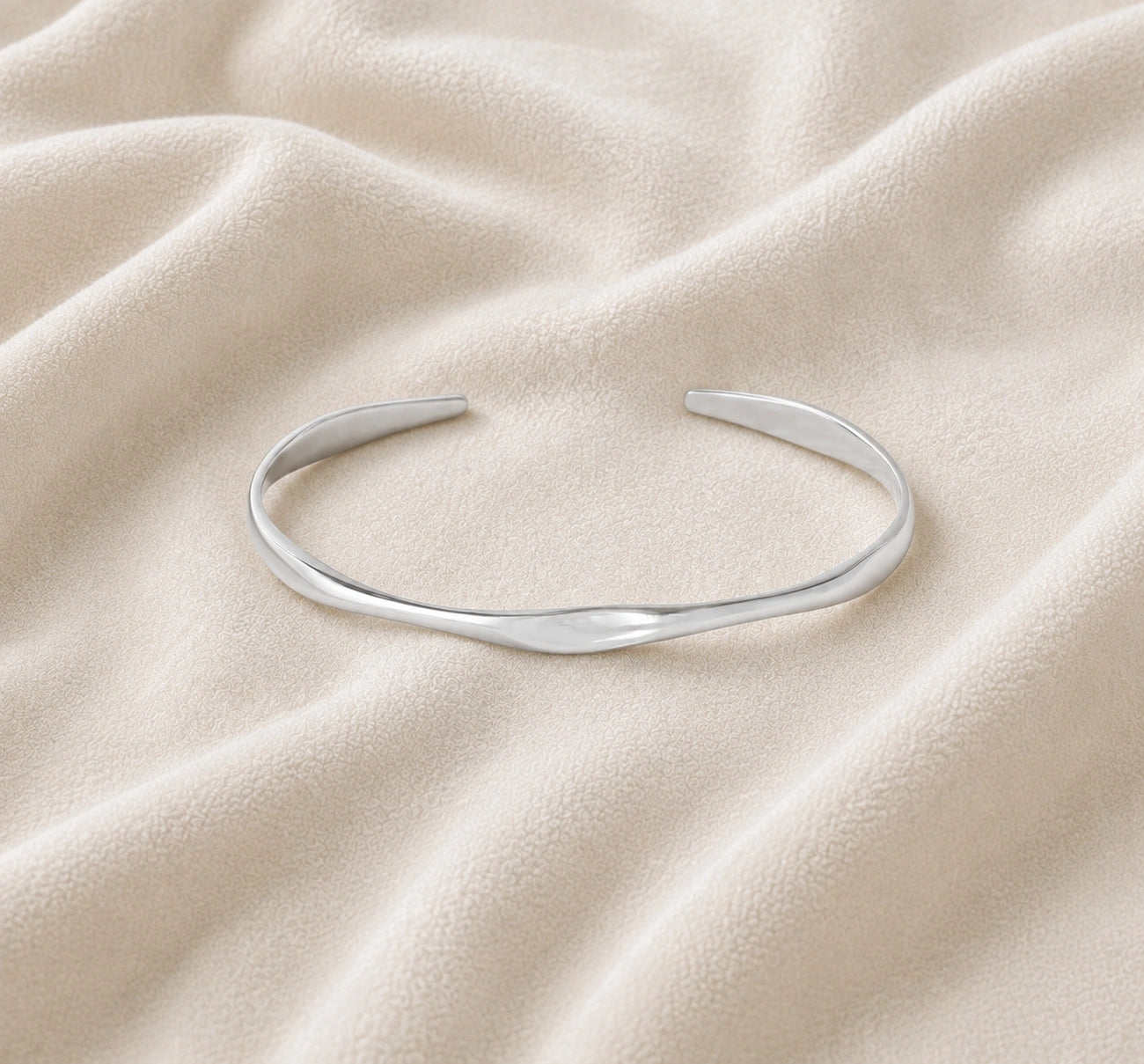Plain_bangle_in_sterling_silver_at_front_angle_view_on_soft_fabric_background