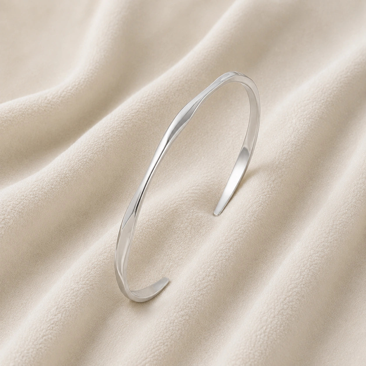 Plain_bangle_in_sterling_silver_at_slight_angle_view_on_soft_fabric_background