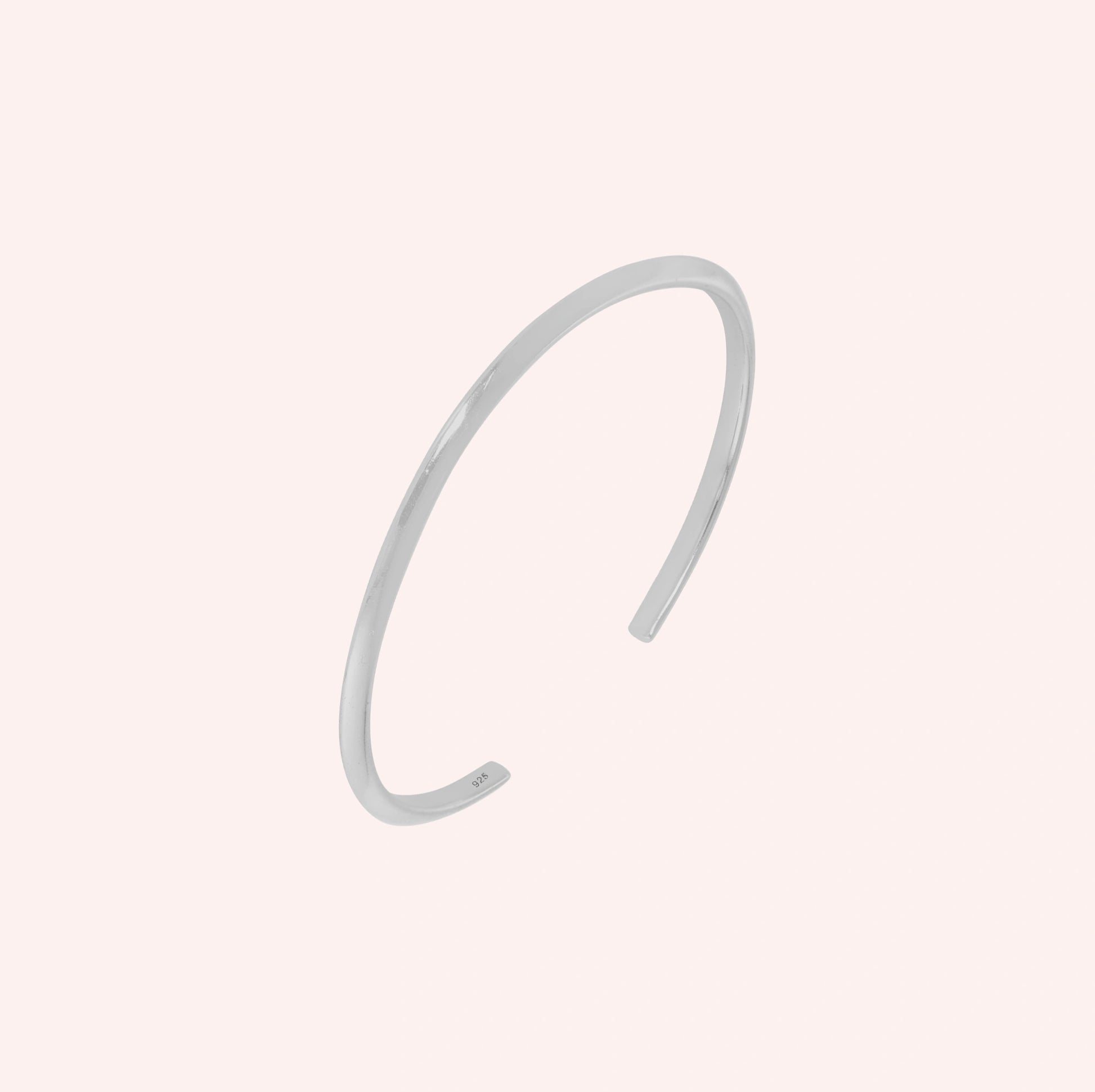 Plain_gold_bangle_in_sterling_silver_at_slight_angle_view_on_solid_pink_background
