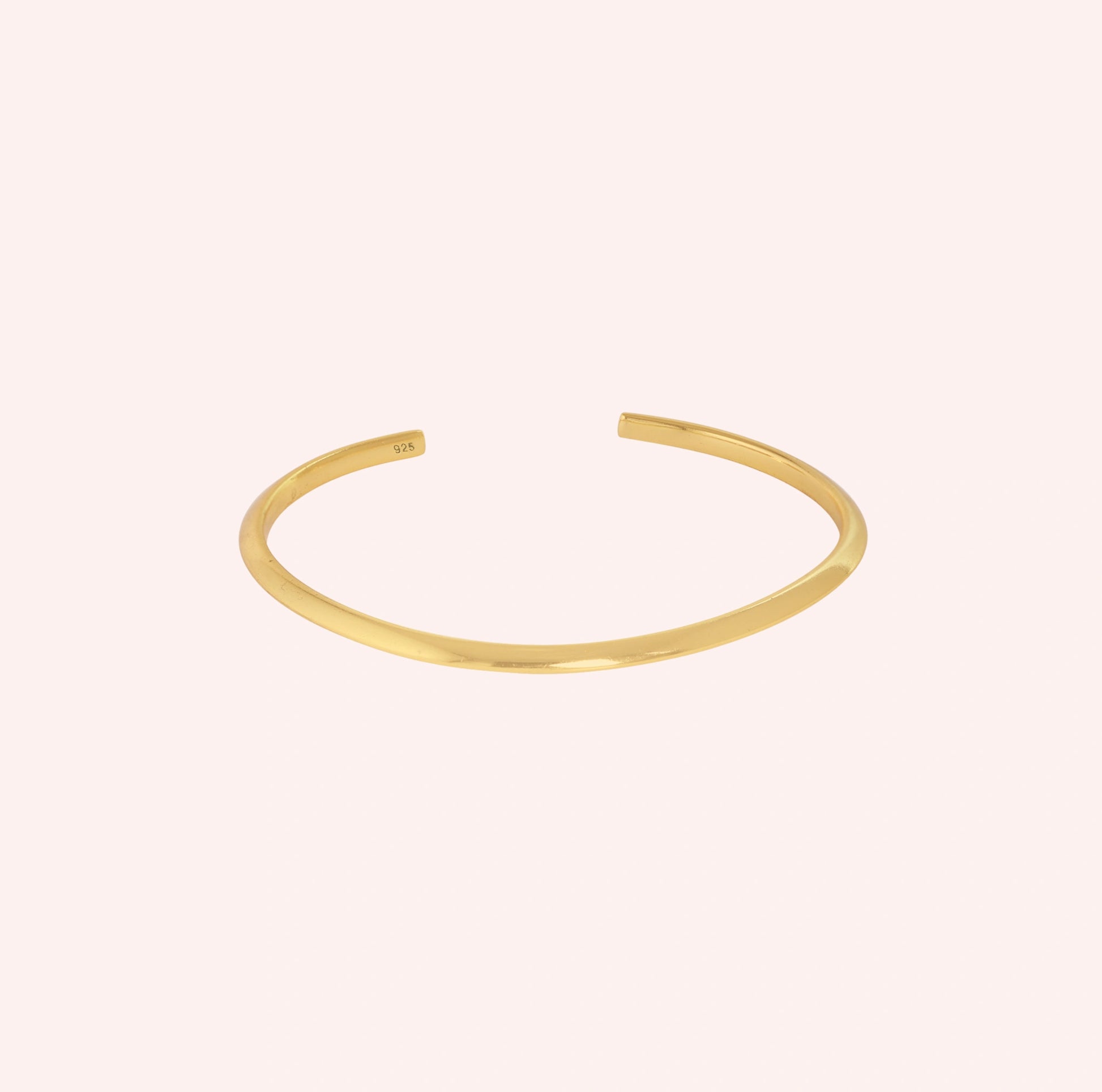 Plain_gold_bangle_in_gold_plated_silver_at_front_angle_view_on_solid_pink_background