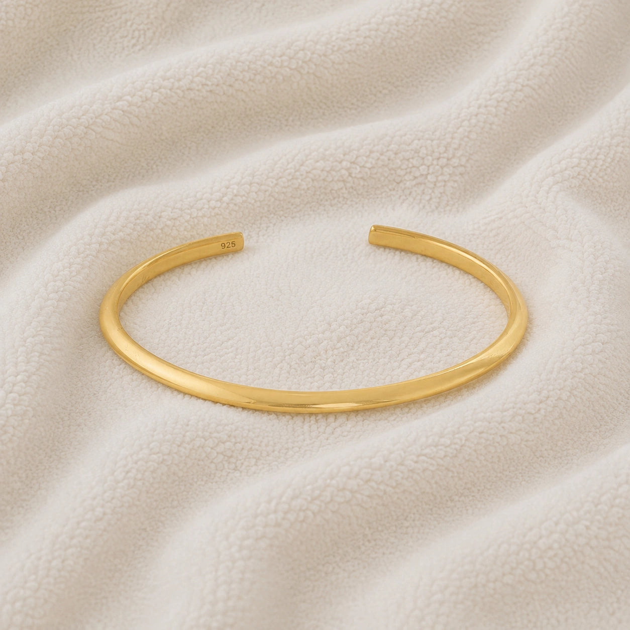Plain_gold_bangle_in_gold_plated_silver_at_front_angle_view_on_soft_fabric_background