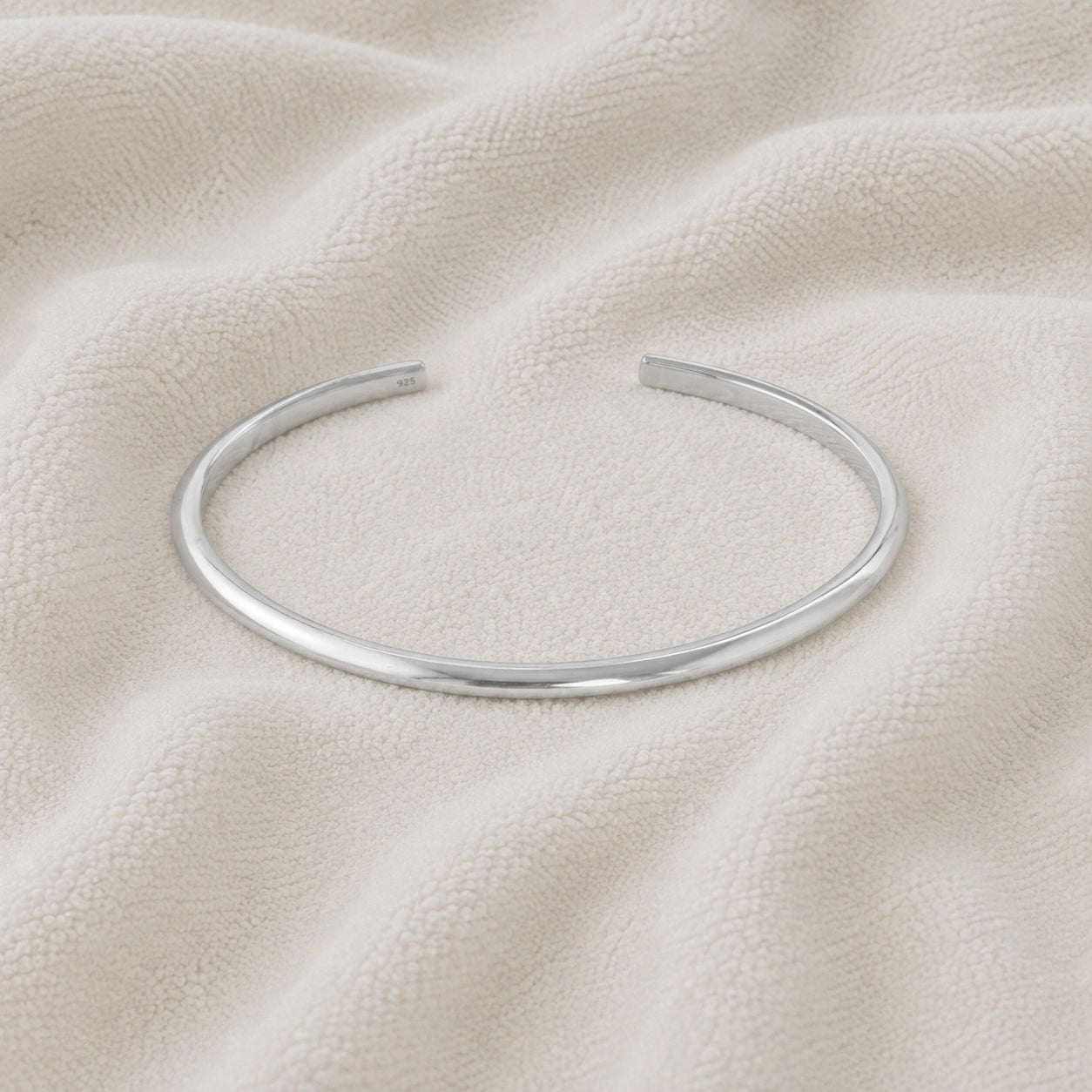 Plain_gold_bangle_in_sterling_silver_at_front_angle_view_on_soft_fabric_background