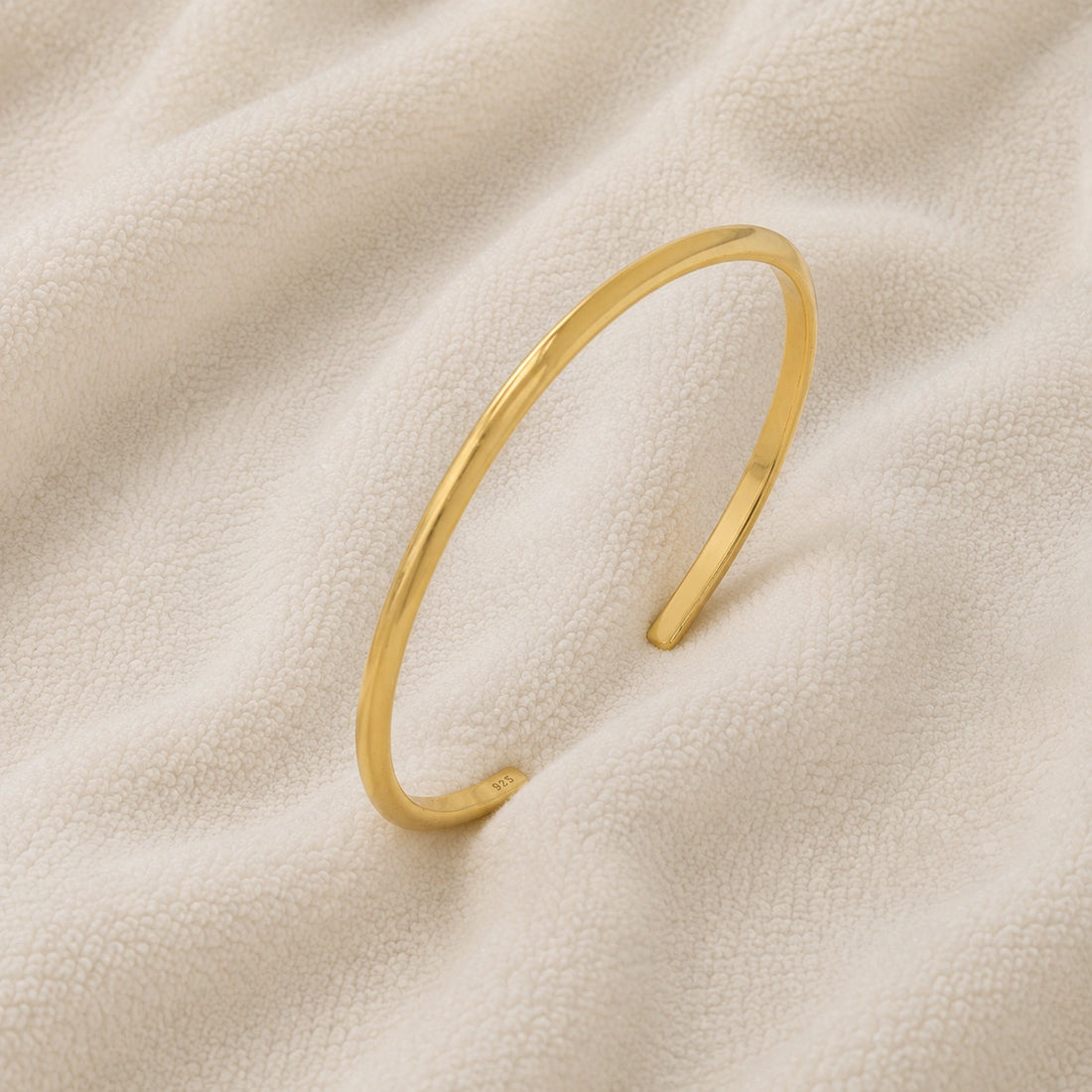 Plain_gold_bangle_in_gold_plated_silver_at_slight_angle_view_on_soft_fabric_background