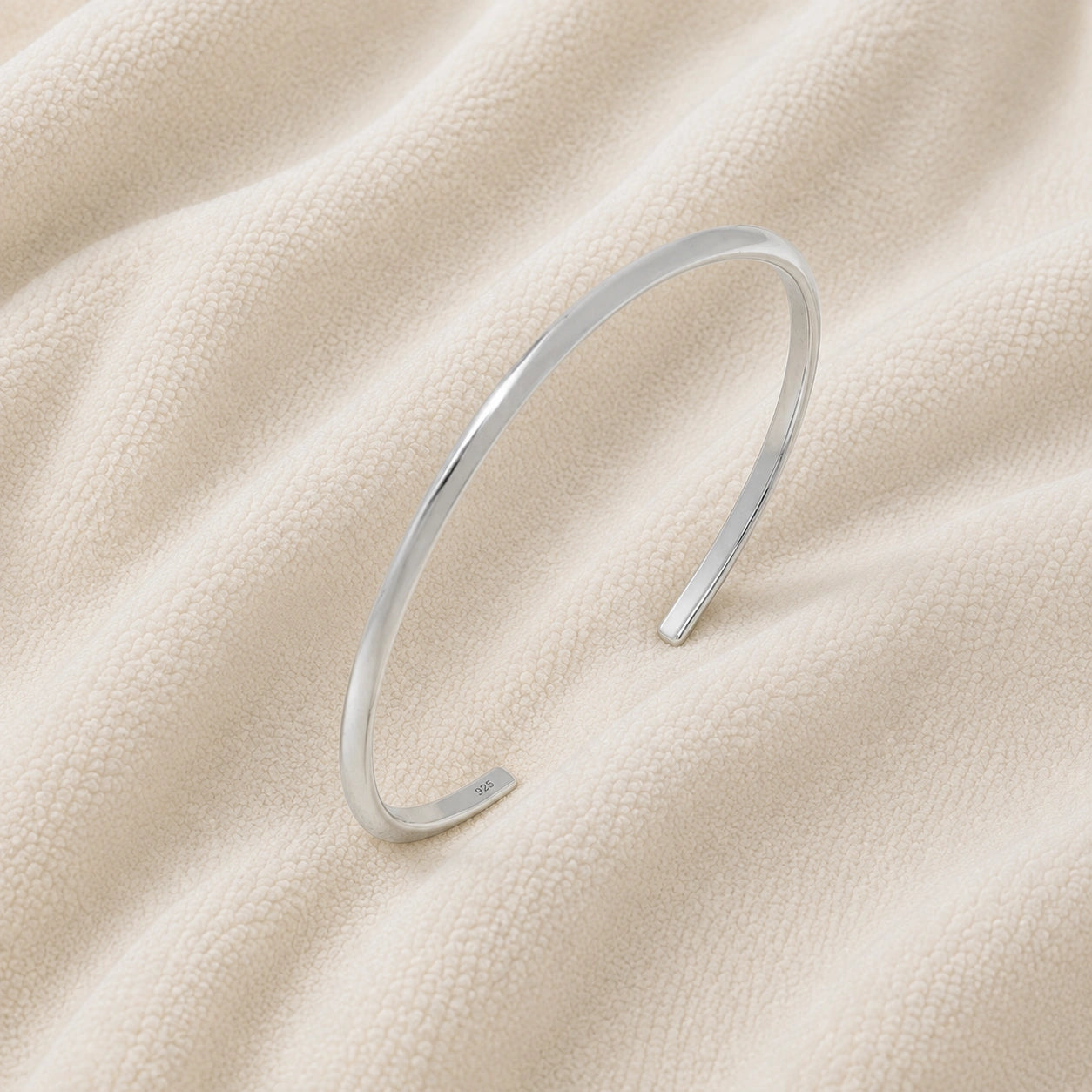 Plain_gold_bangle_in_sterling_silver_at_slight_angle_view_on_soft_fabric_background