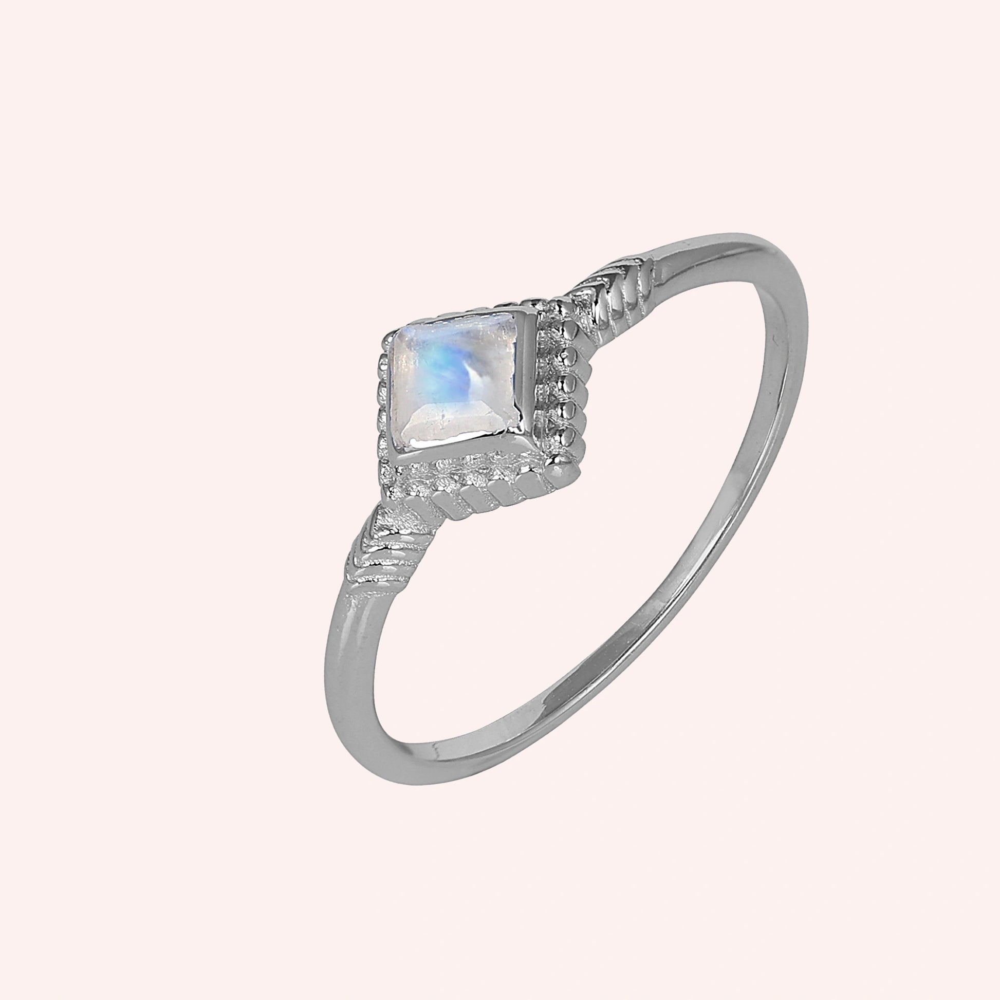 Princess_cut_ring_sterling_silver_with_square_moonstone_and_detailed_band_slightly_tilted_view_on_solid_pink_background