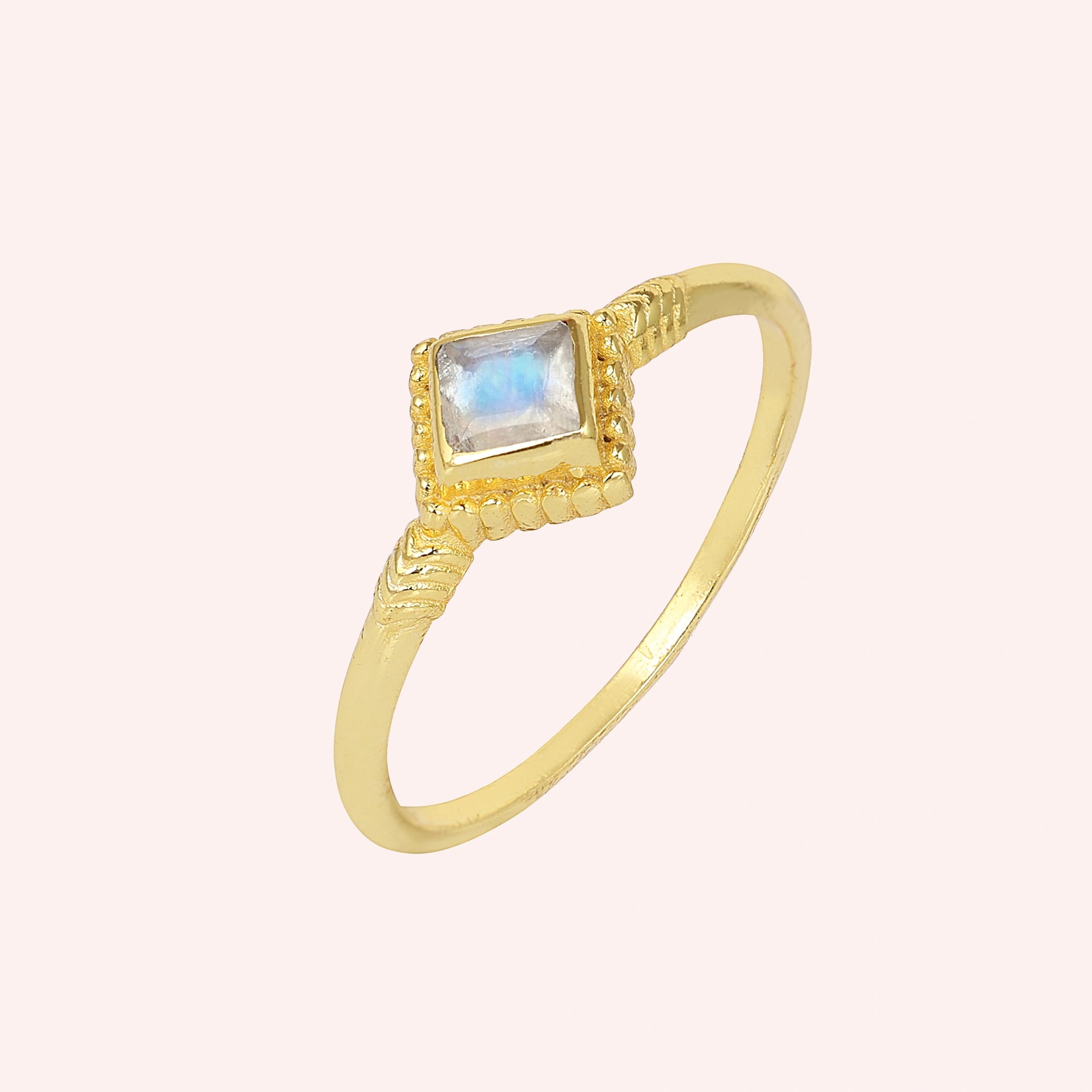 Princess_cut_ring_gold_plated_silver_with_square_moonstone_and_detailed_band_slightly_tilted_view_on_solid_pink_background
