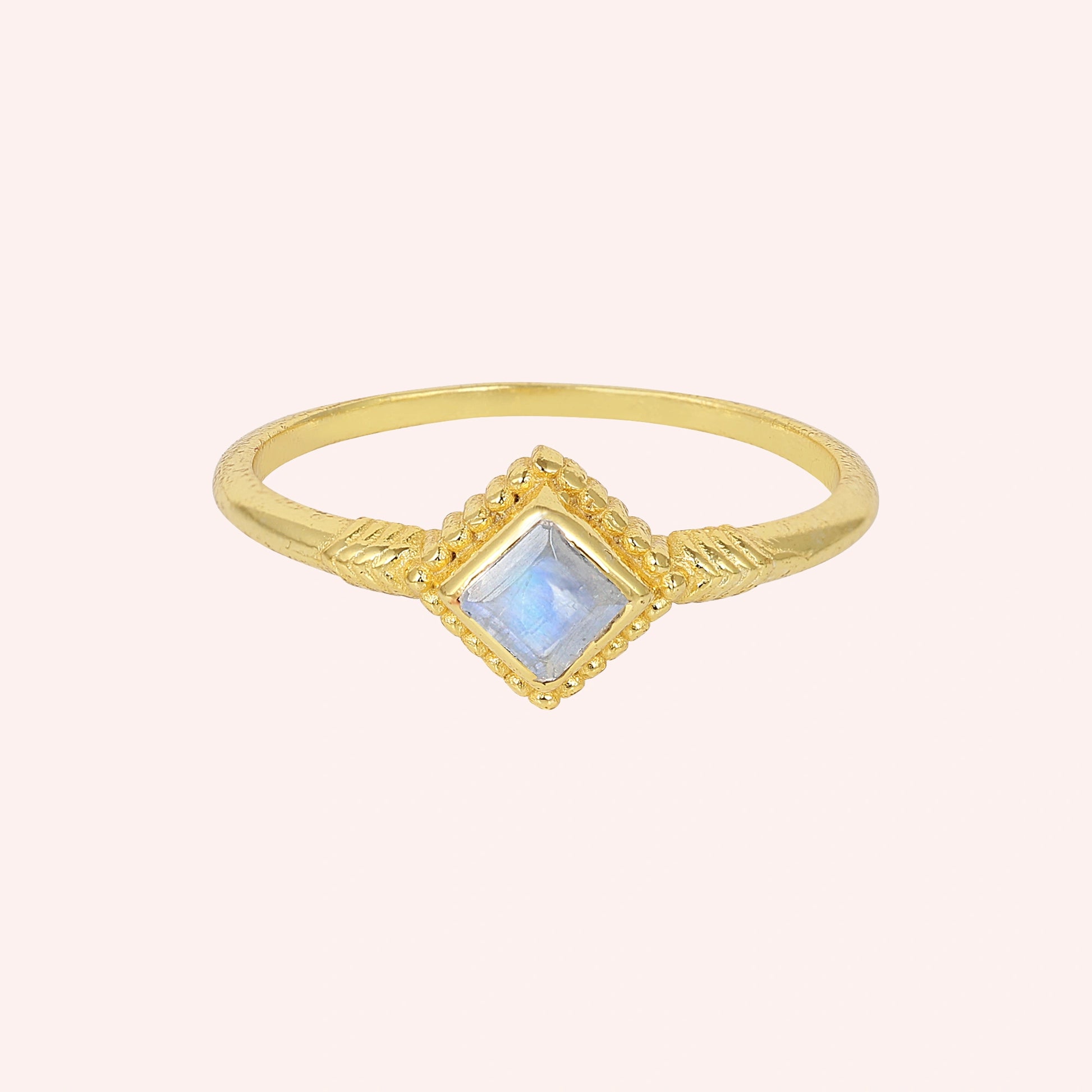Princess_cut_ring_gold_plated_silver_with_square_moonstone_and_detailed_band_front_angle_view_on_solid_pink_background