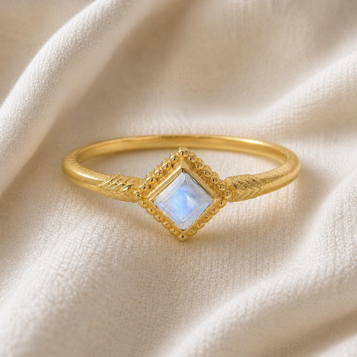 Princess_cut_ring_gold_plated_silver_with_square_moonstone_and_detailed_band_front_angle_view_on_soft_fabric_background
