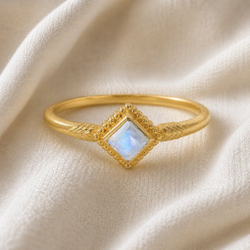 Princess_cut_ring_gold_plated_silver_with_square_moonstone_and_detailed_band_front_angle_view_on_soft_fabric_background