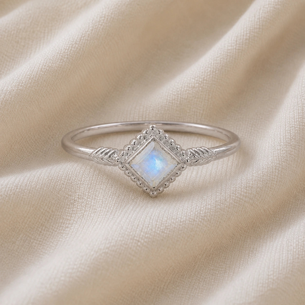 Princess_cut_ring_sterling_silver_with_square_moonstone_and_detailed_band_front_angle_view_on_soft_fabric_background