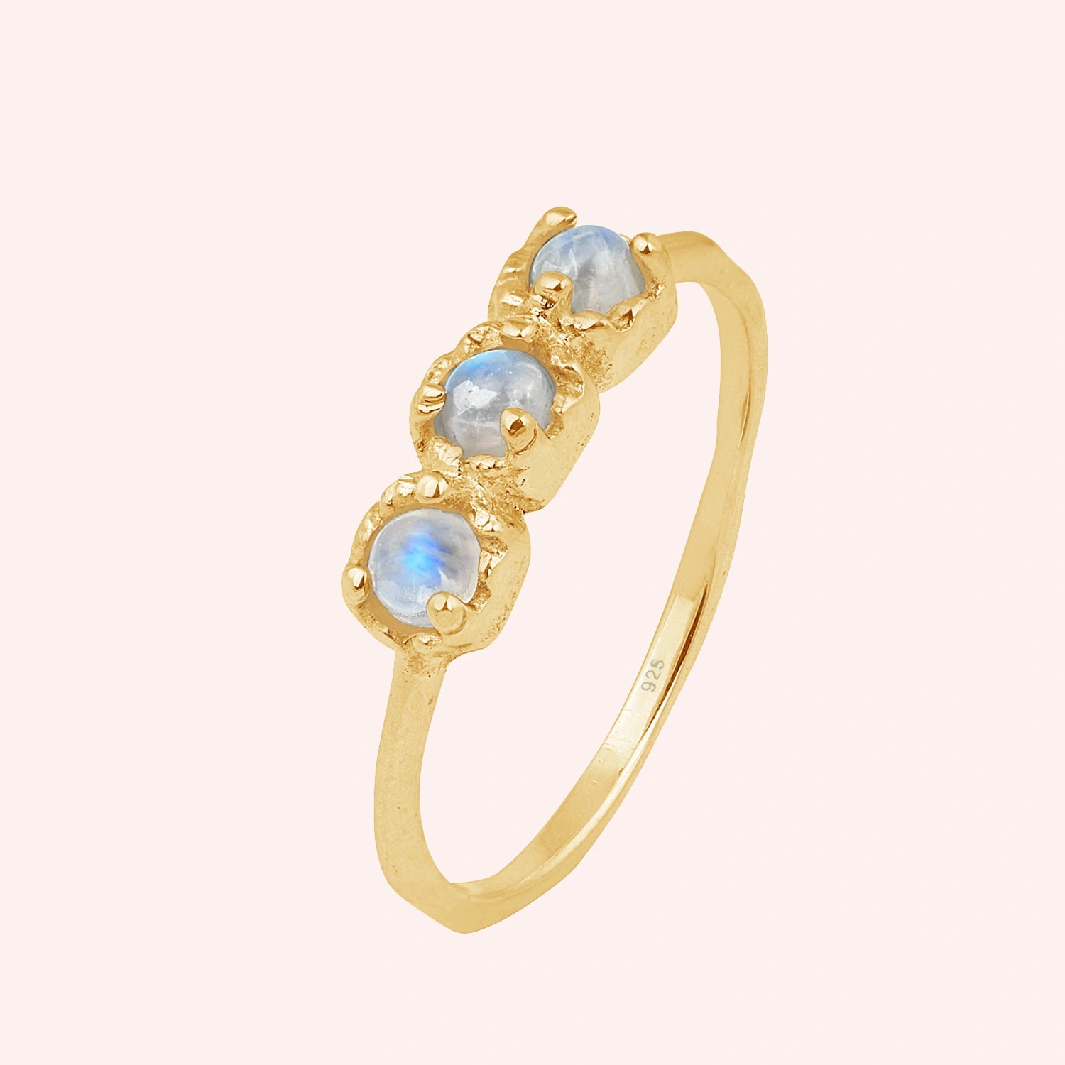 Rainbow_moonstone_ring_in_gold_plated_silver_with_three_moonstones_at_slight_angle_on_solid_pink_background