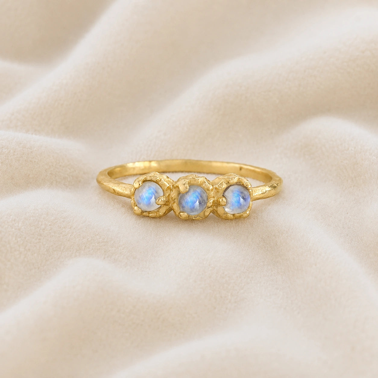 Rainbow_moonstone_ring_in_gold_plated_silver_with_three_moonstones_at_front_angle_on_soft_fabric_background