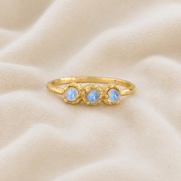 Rainbow_moonstone_ring_in_gold_plated_silver_with_three_moonstones_at_front_angle_on_soft_fabric_background