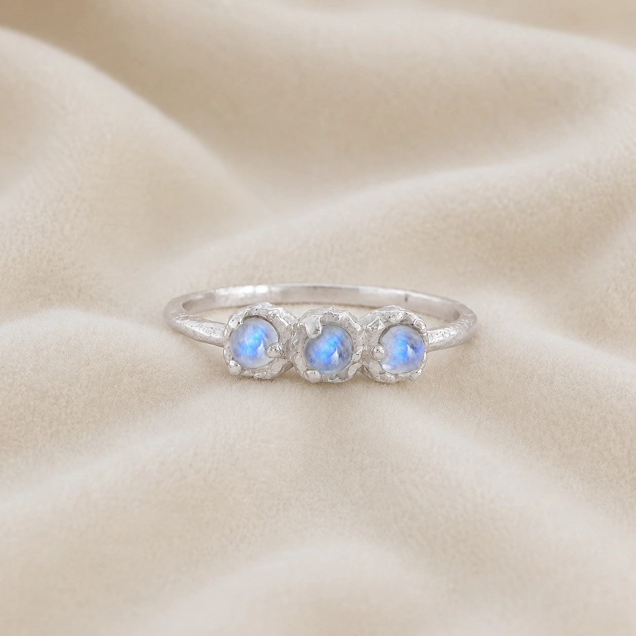 Rainbow_moonstone_ring_in_sterling_silver_with_three_moonstones_at_front_angle_on_soft_fabric_background