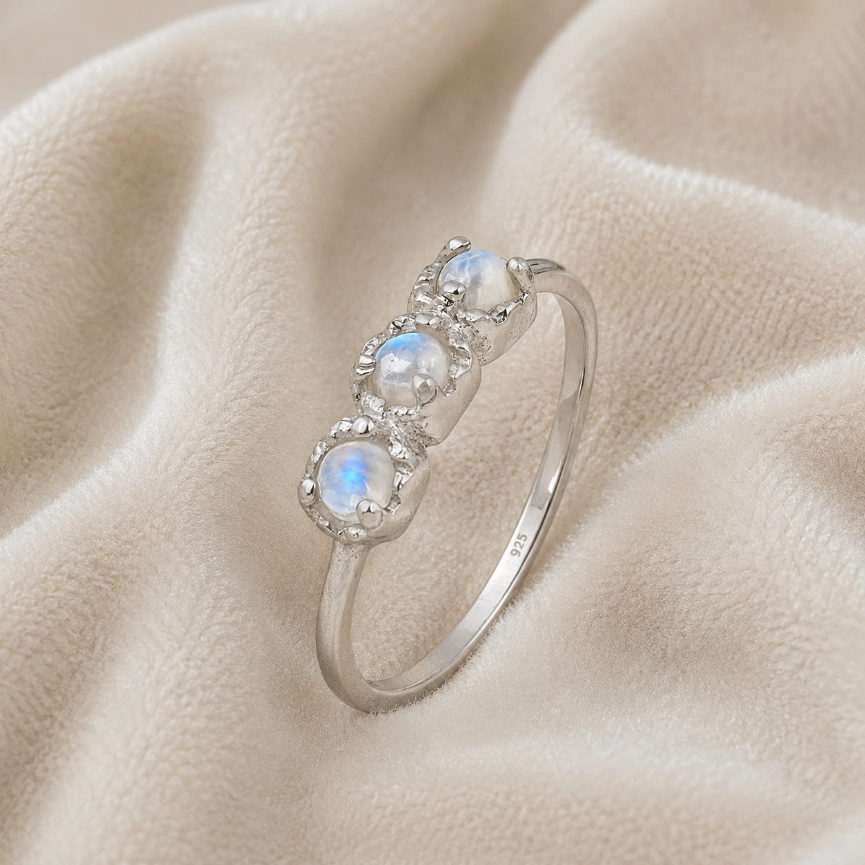 Rainbow_moonstone_ring_in_sterling_silver_with_three_moonstones_at_slight_angle_on_soft_fabric_background