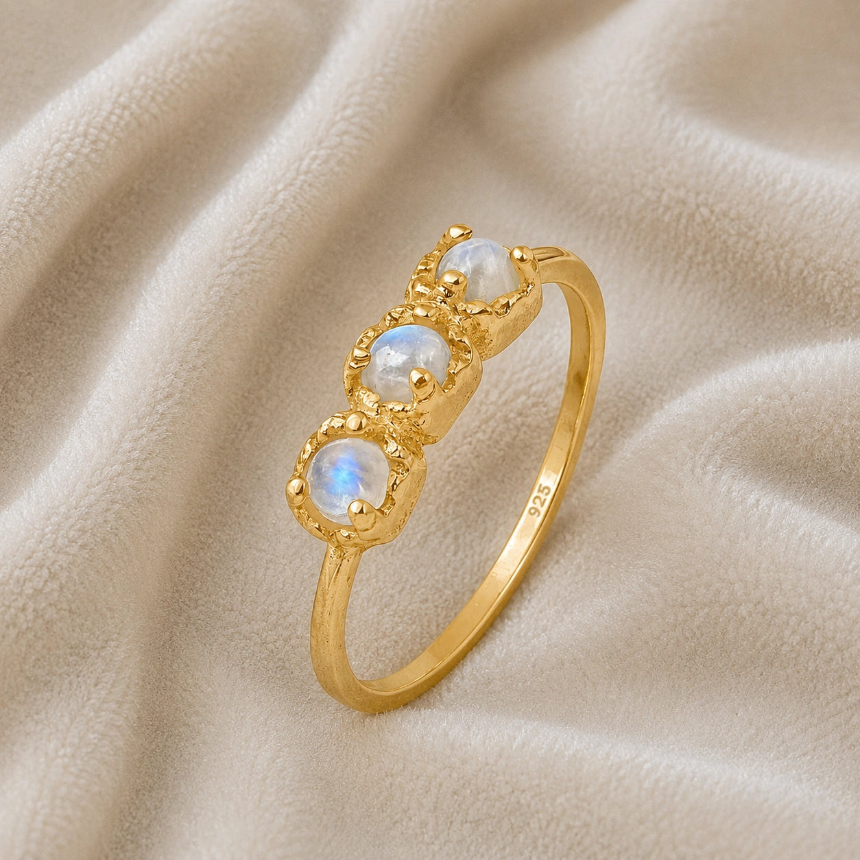 Rainbow_moonstone_ring_in_gold_plated_silver_with_three_moonstones_at_slight_angle_on_soft_fabric_background