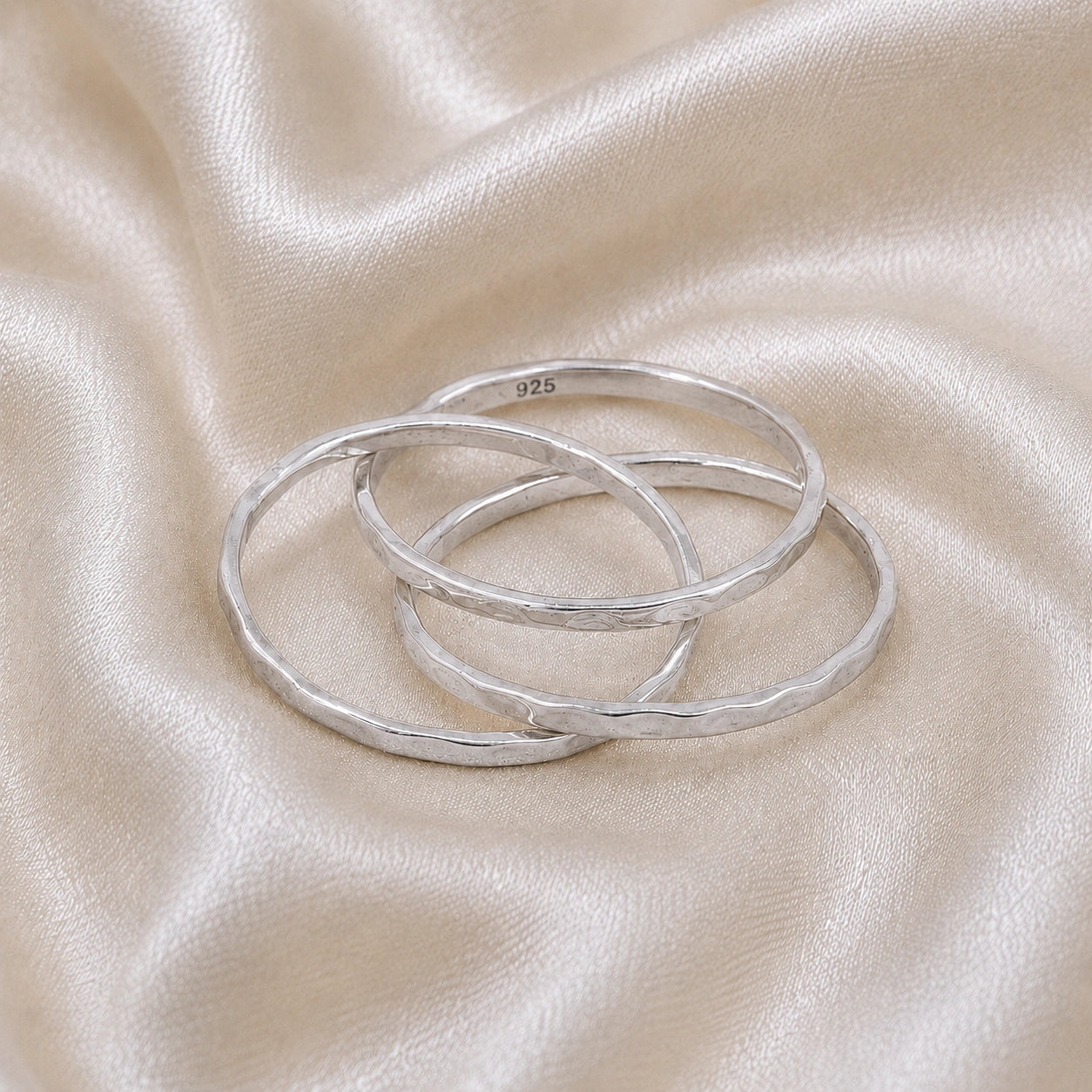 Ring_set_of_three_sterling_silver_textured_stacking_bands_at_front_angle_on_soft_fabric_background