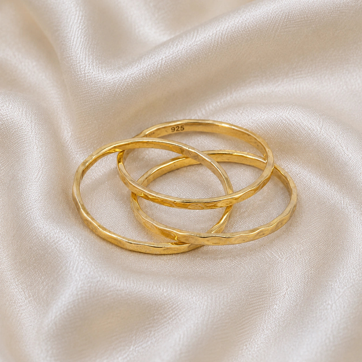 Ring_set_of_three_gold_plated_silver_textured_stacking_bands_at_front_angle_on_soft_fabric_background
