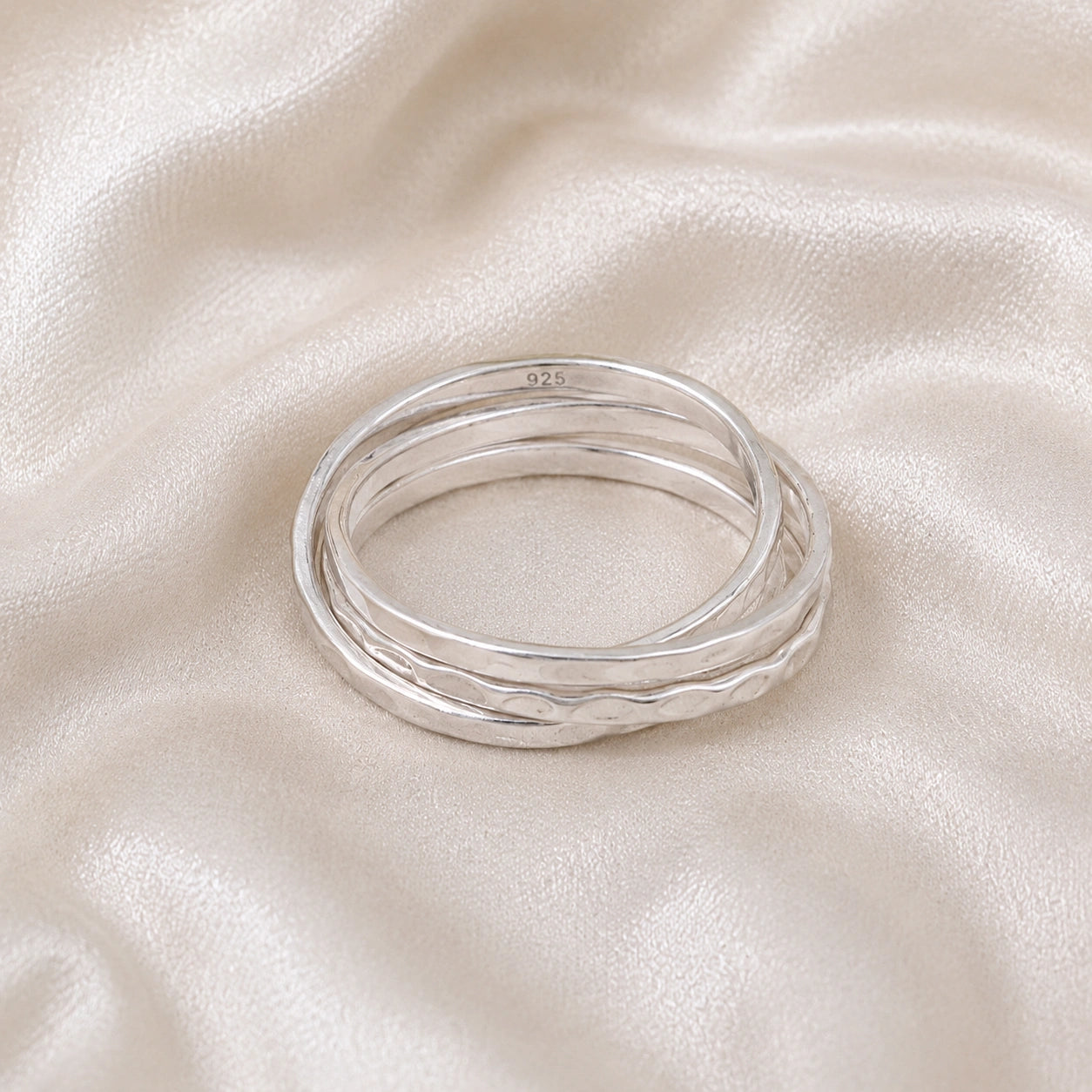 Ring_set_of_three_sterling_silver_textured_stacking_bands_at_front_angle_on_soft_fabric_background