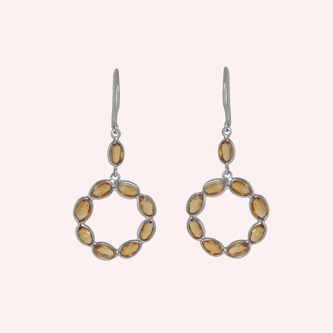 Round_earrings_in_gold_plated_silver_with_oval_citrine_stones_at_front_angle_view_on_solid_pink_background