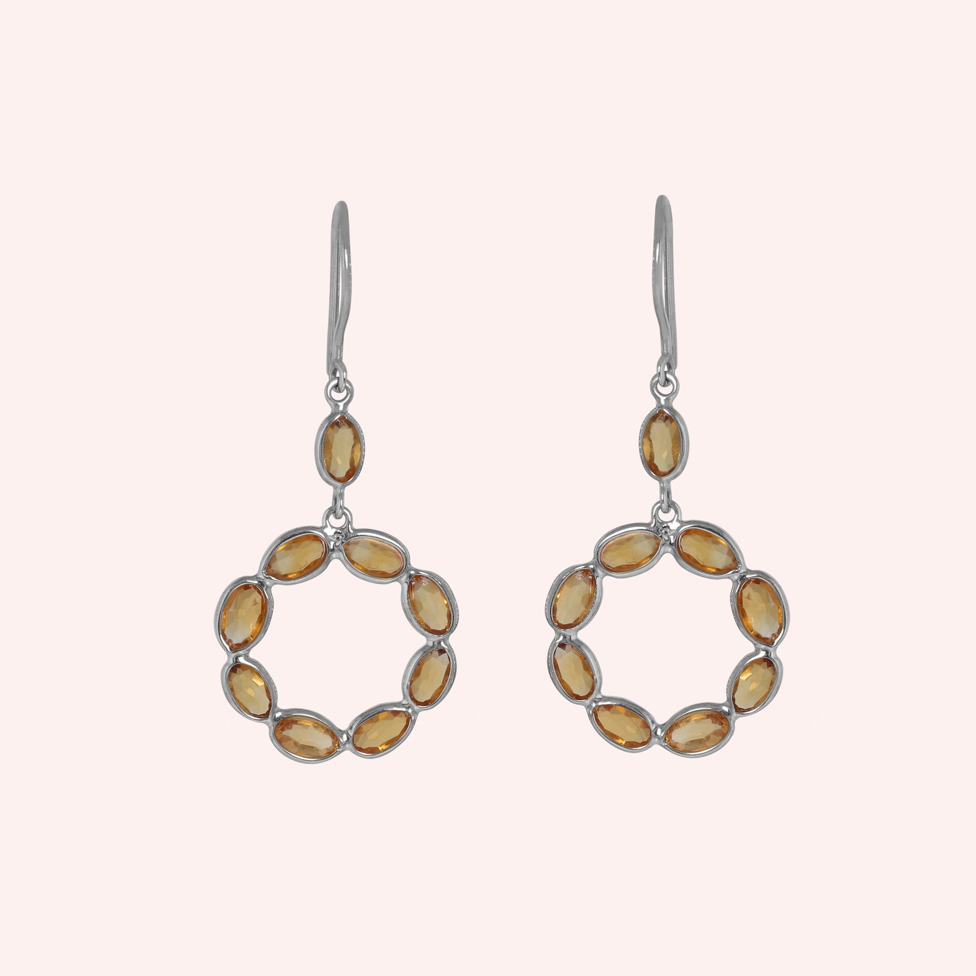 Round_earrings_in_sterling_silver_with_oval_citrine_stones_at_front_angle_view_on_solid_pink_background