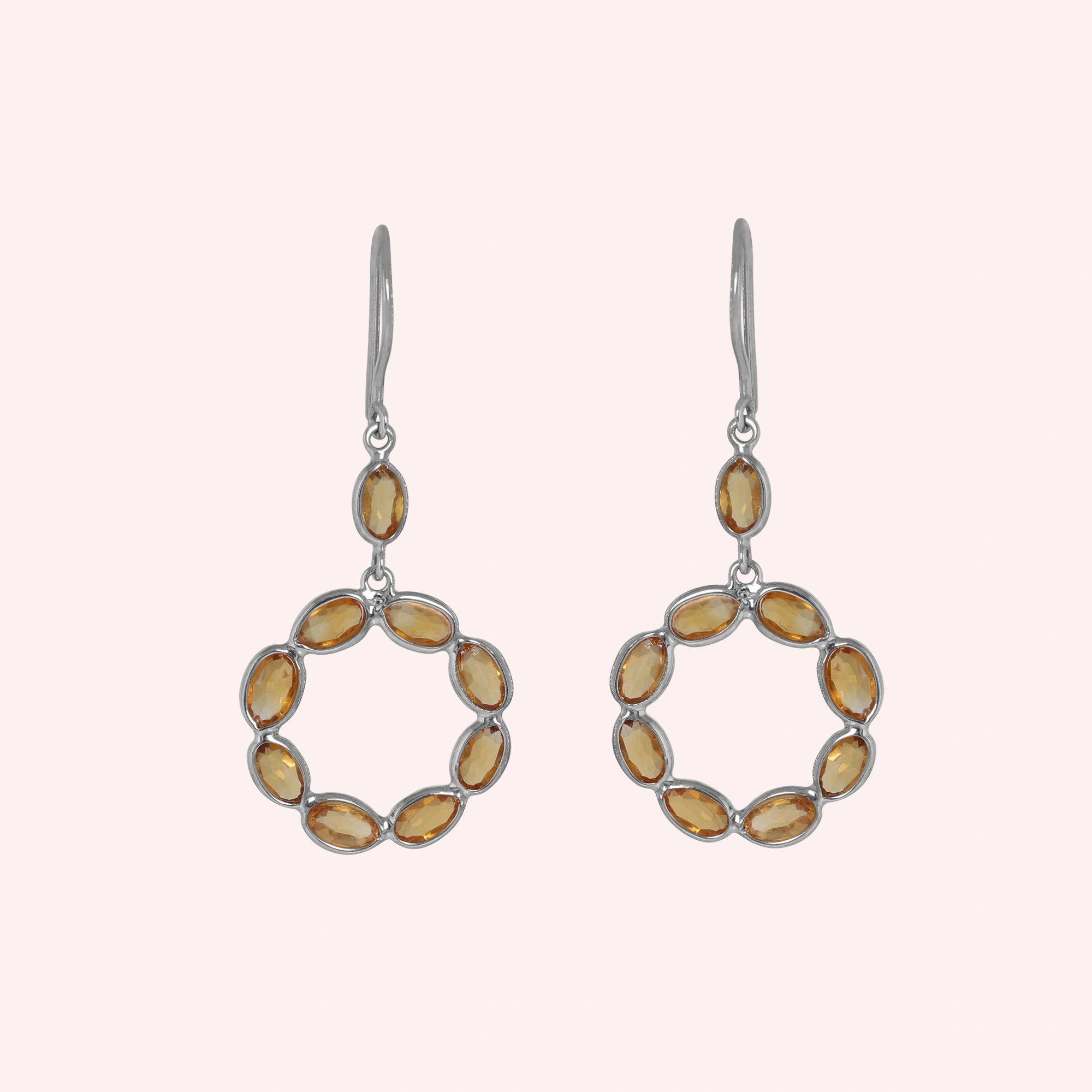 Round_earrings_in_sterling_silver_with_oval_citrine_stones_at_front_angle_view_on_solid_pink_background