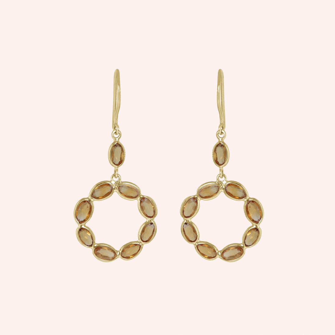 Round_earrings_in_gold_plated_silver_with_oval_citrine_stones_at_front_angle_view_on_solid_pink_background