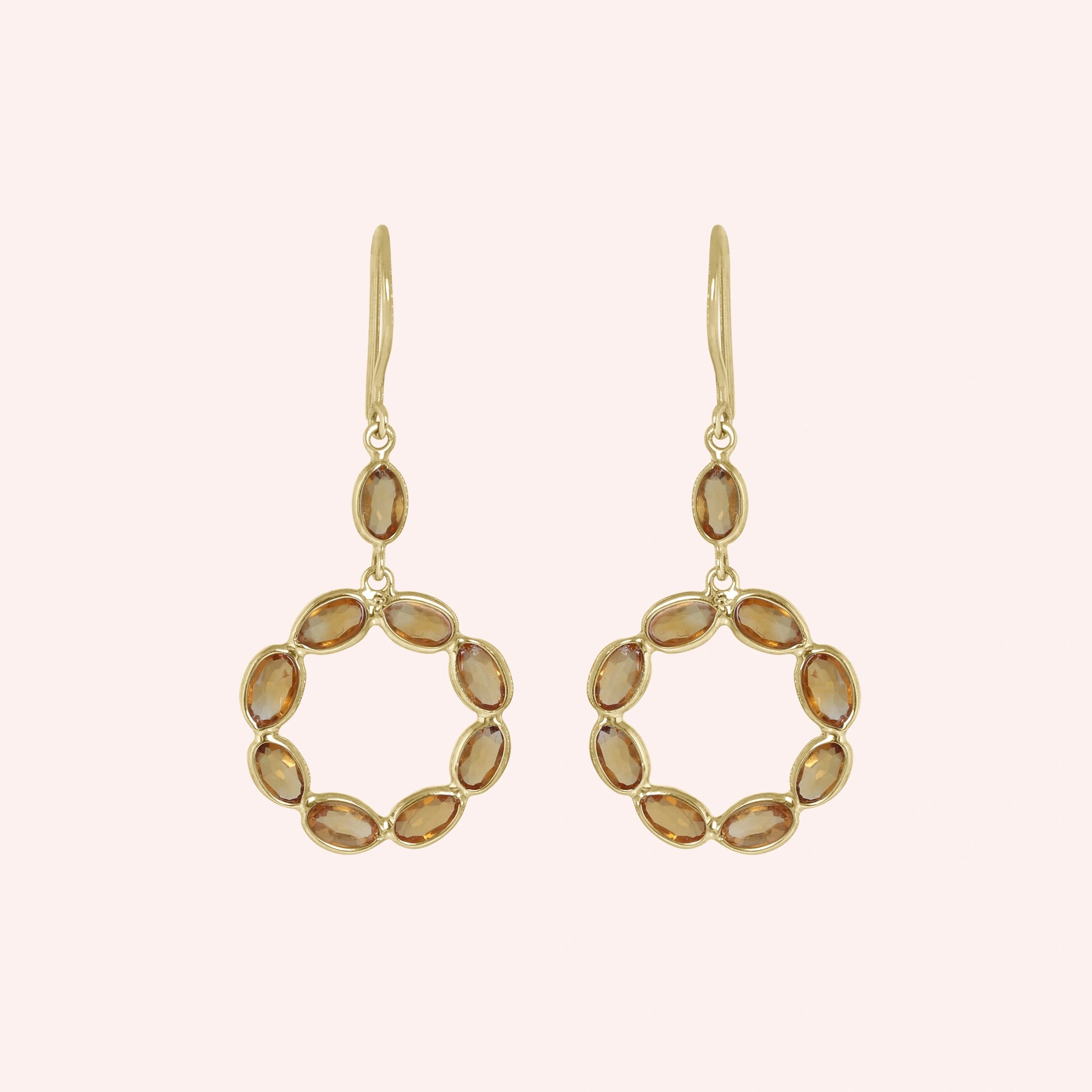 Round_earrings_in_gold_plated_silver_with_oval_citrine_stones_at_front_angle_view_on_solid_pink_background