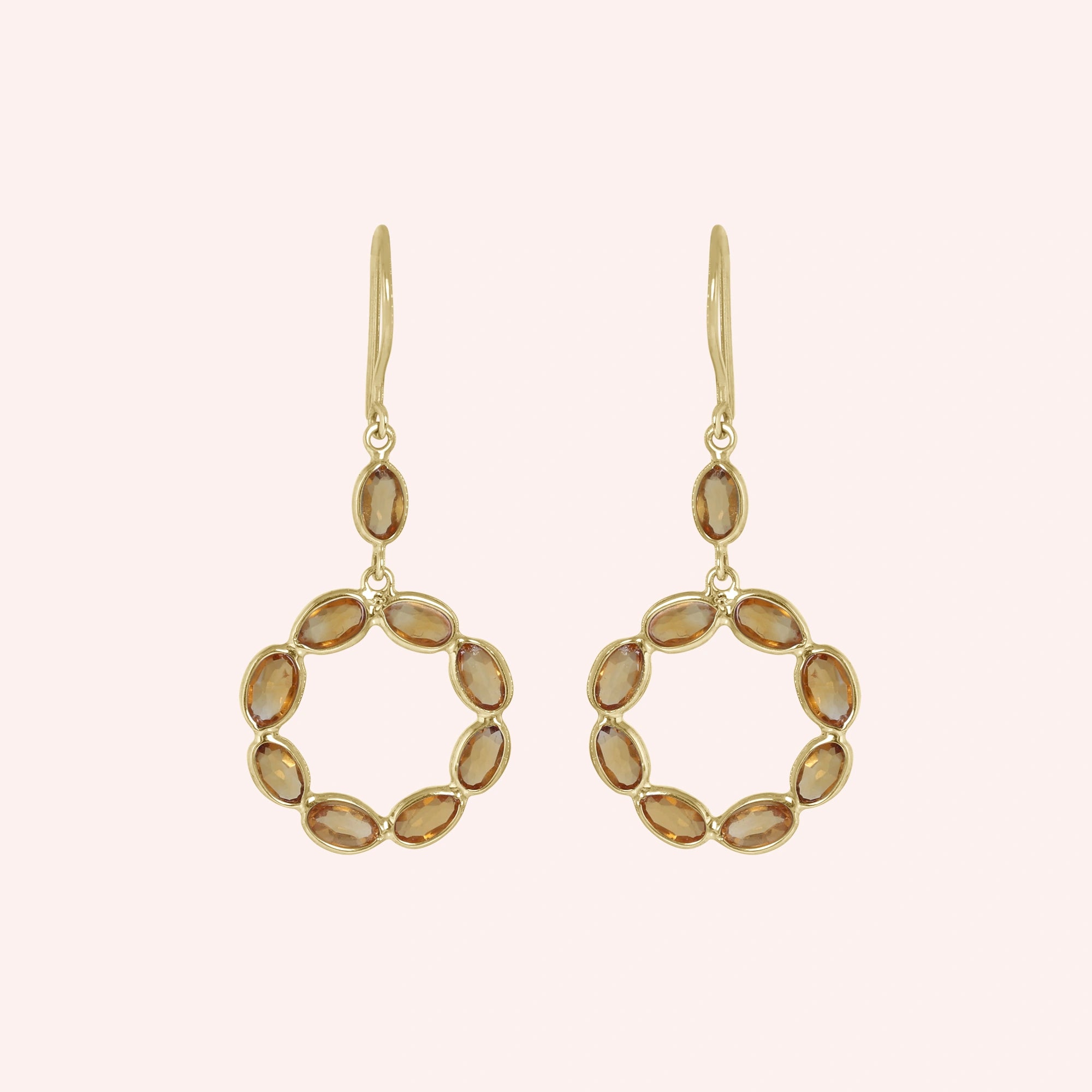 Round_earrings_in_gold_plated_silver_with_oval_citrine_stones_at_front_angle_view_on_solid_pink_background