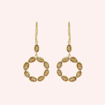 Round_earrings_in_gold_plated_silver_with_oval_citrine_stones_at_front_angle_view_on_solid_pink_background
