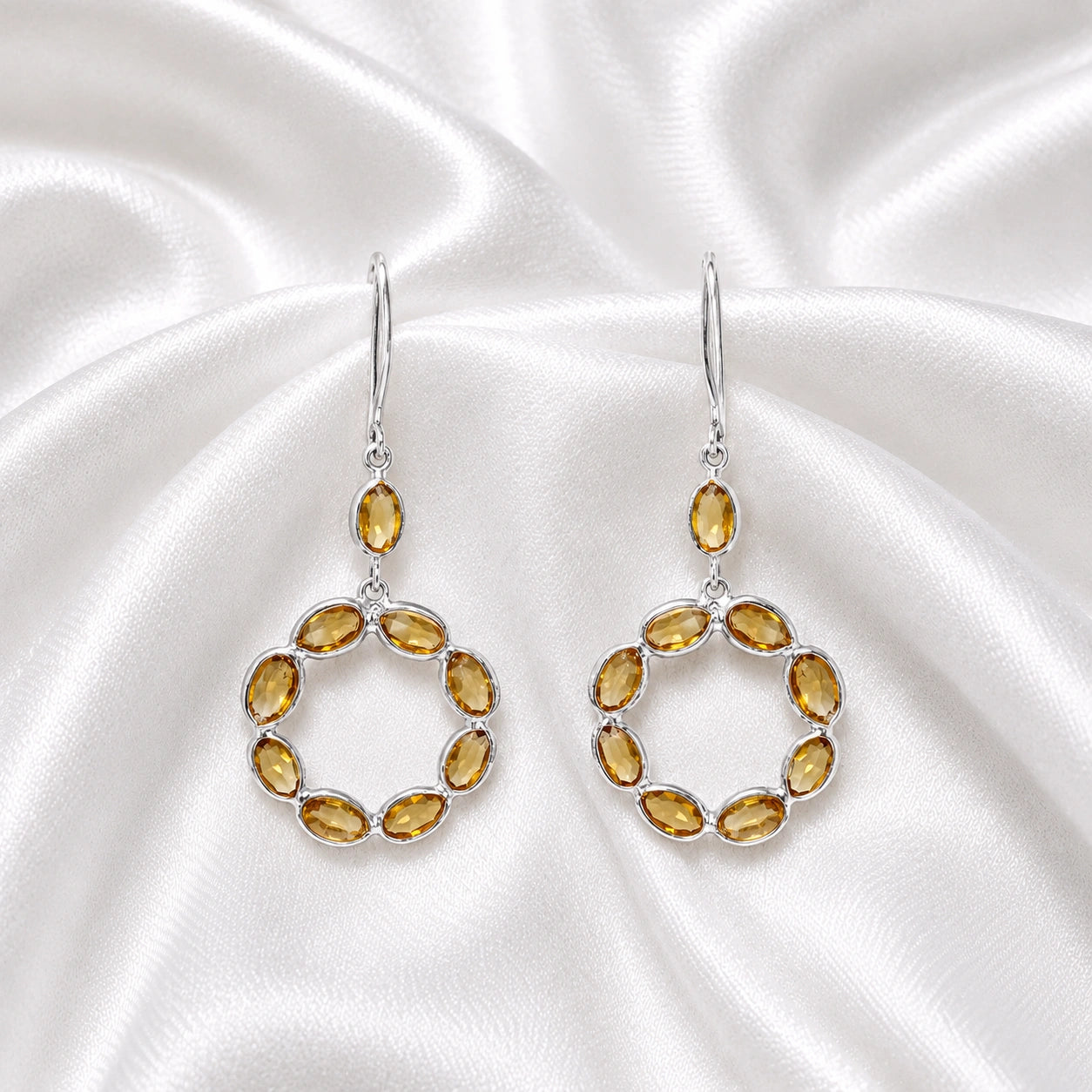 Round_earrings_in_sterling_silver_with_oval_citrine_stones_at_front_angle_view_on_soft_fabric_background