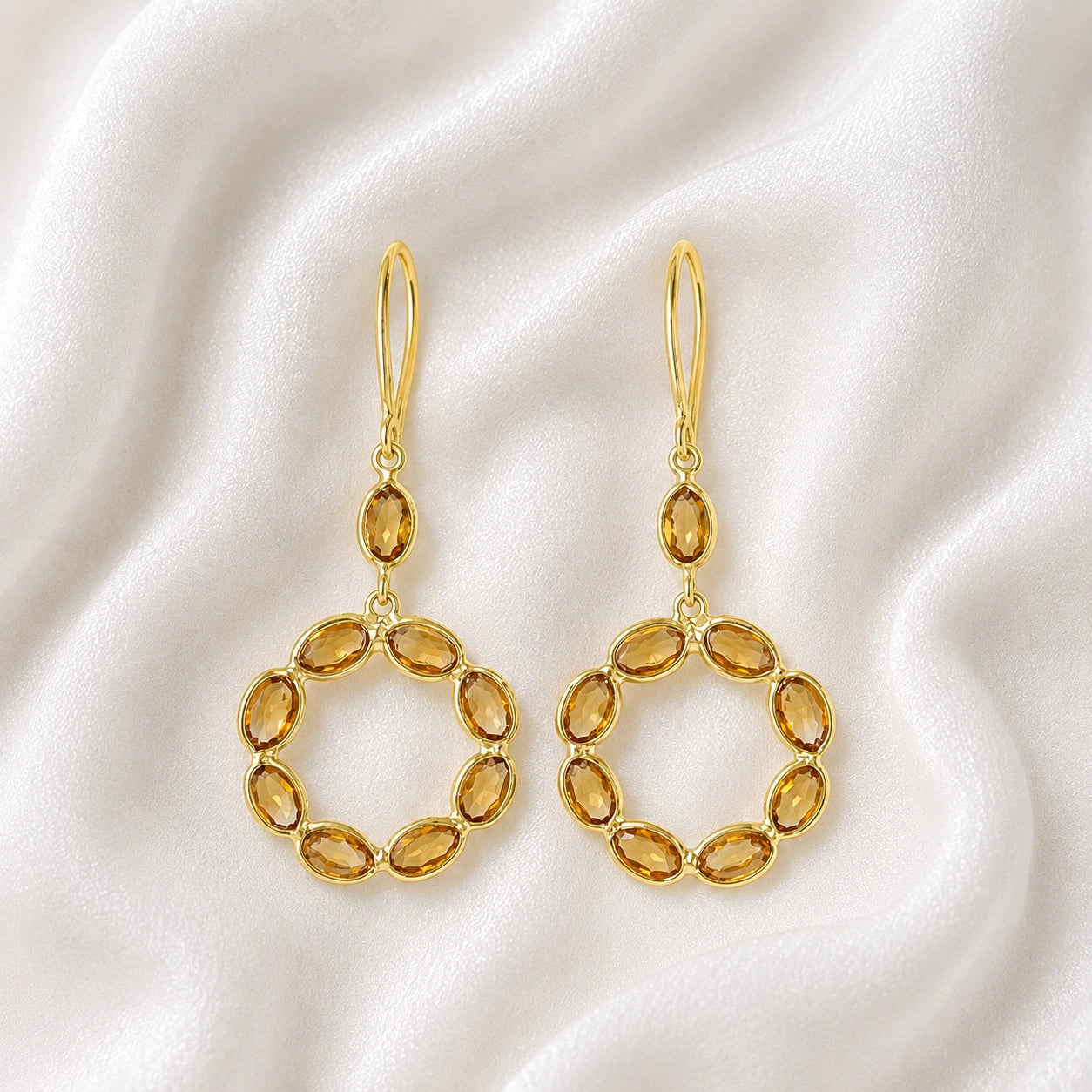 Round_earrings_in_gold_plated_silver_with_oval_citrine_stones_at_front_angle_view_on_soft_fabric_background