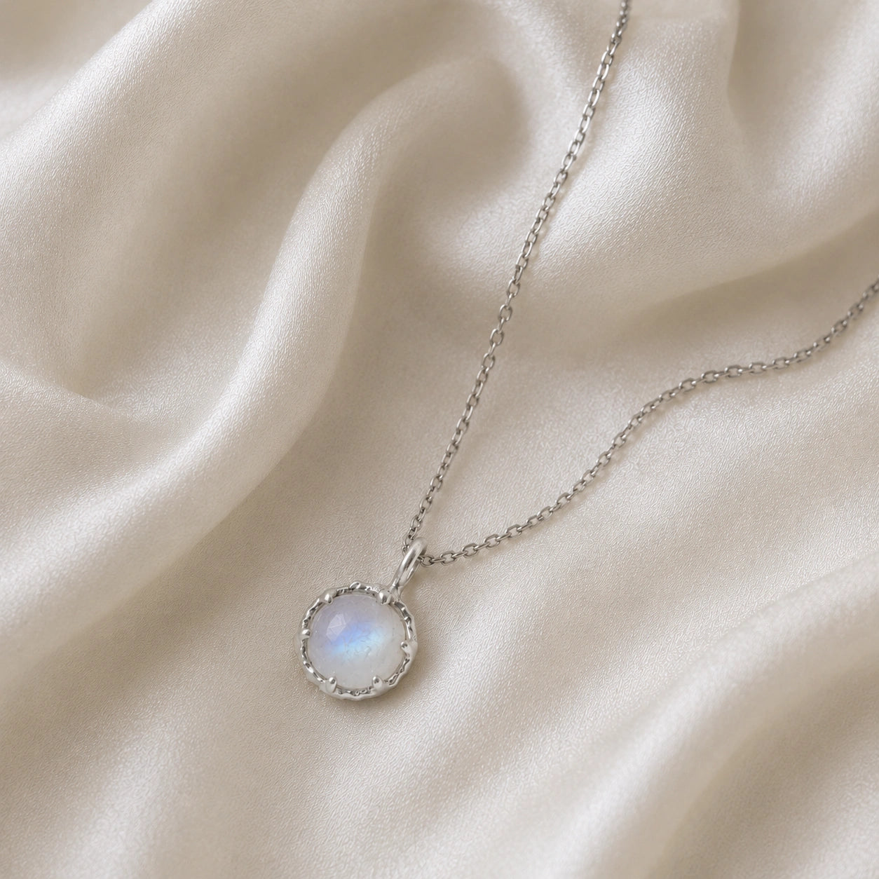 Round_necklace_in_sterling_silver_slightly_angled_featuring_round_moonstone_on_a_soft_fabric_background