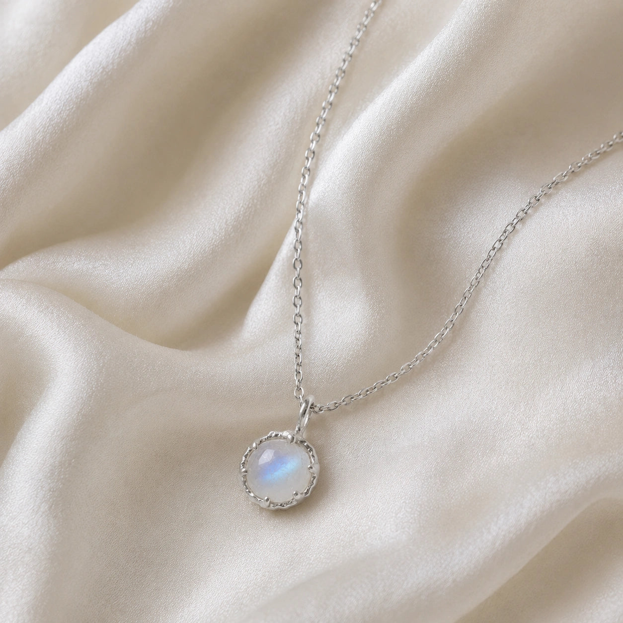 Round_necklace_in_sterling_silver_at_front_angle_featuring_round_moonstone_on_a_soft_fabric_background
