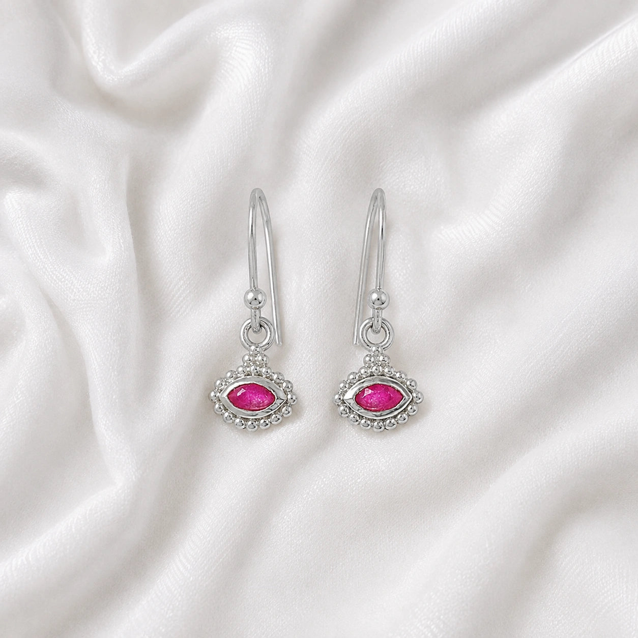 Ruby_earrings_in_sterling_silver_with_marquise_ruby_stone_at_frontt_angle_view_on_soft_fabric_background