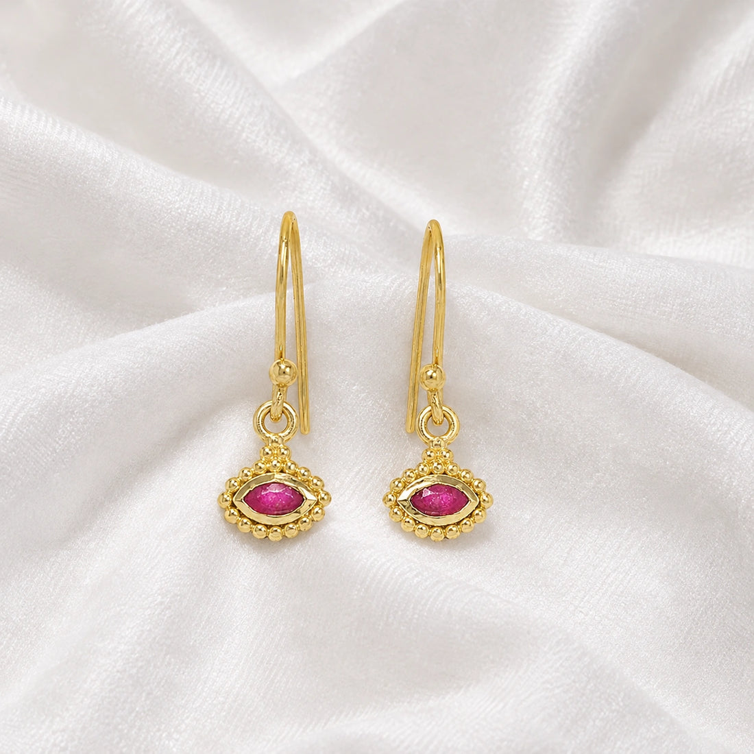 Ruby_earrings_in_gold_plated_silver_with_marquise_ruby_stone_at_front_angle_view_on_soft_fabric_background