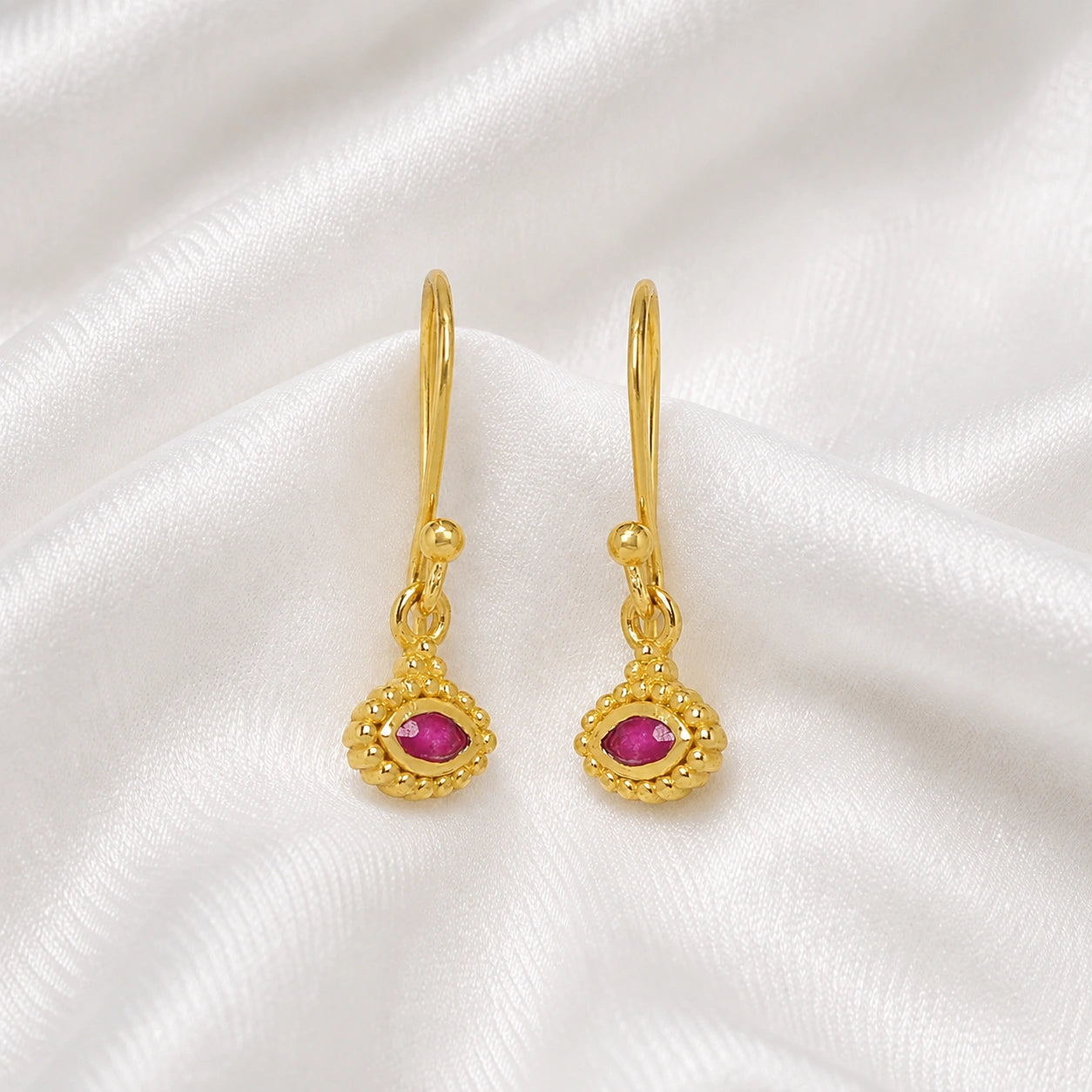 Ruby_earrings_in_gold_plated_silver_with_marquise_ruby_stone_at_slight_angle_view_on_soft_fabric_background