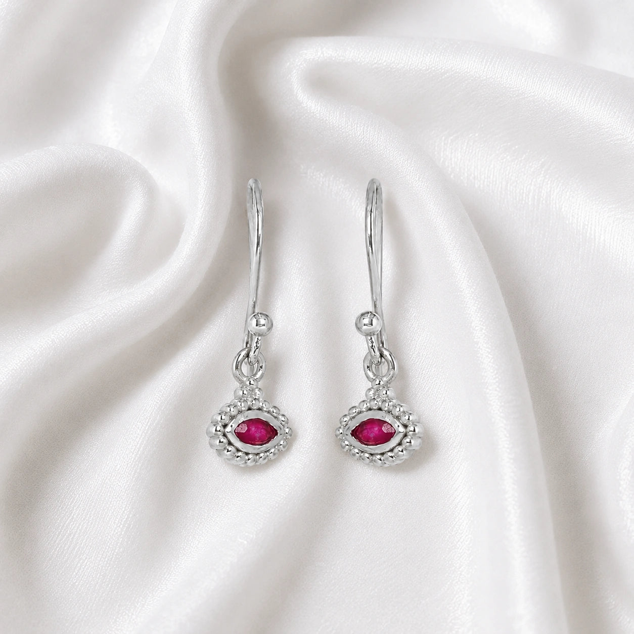 Ruby_earrings_in_sterling_silver_with_marquise_ruby_stone_at_slight_angle_view_on_soft_fabric_background