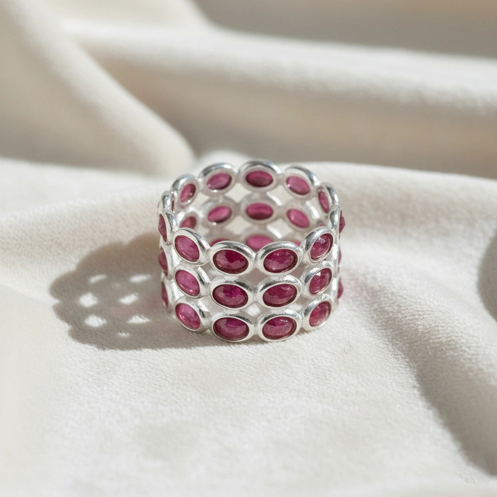 Silver ruby eternity ring band featuring three rows of oval-cut rubies on a white velvet fabric background from a slight angle.
